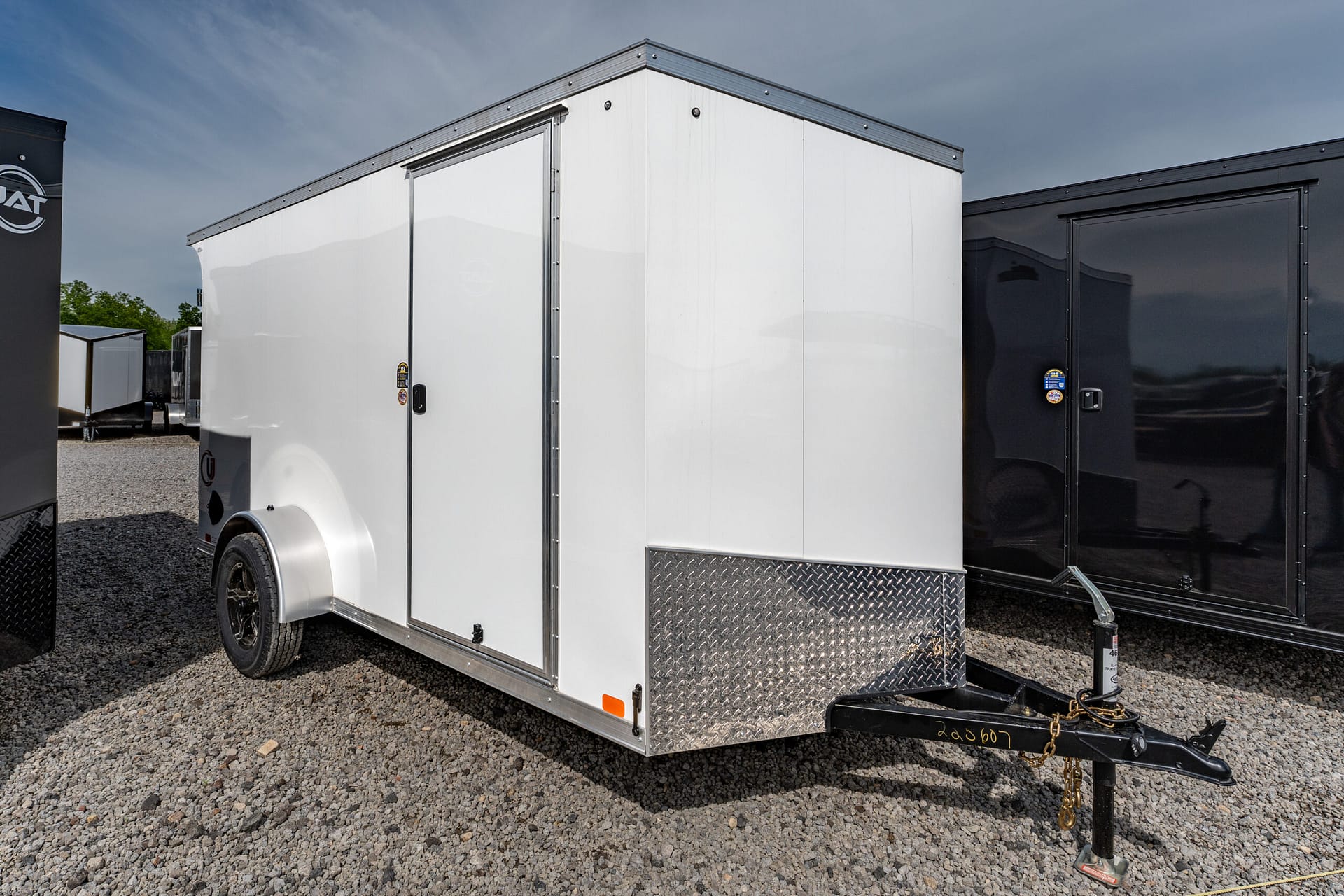White enclosed cargo trailer on a gravel lot, featuring diamond-plate metal at the edge and a visible hitch in front.