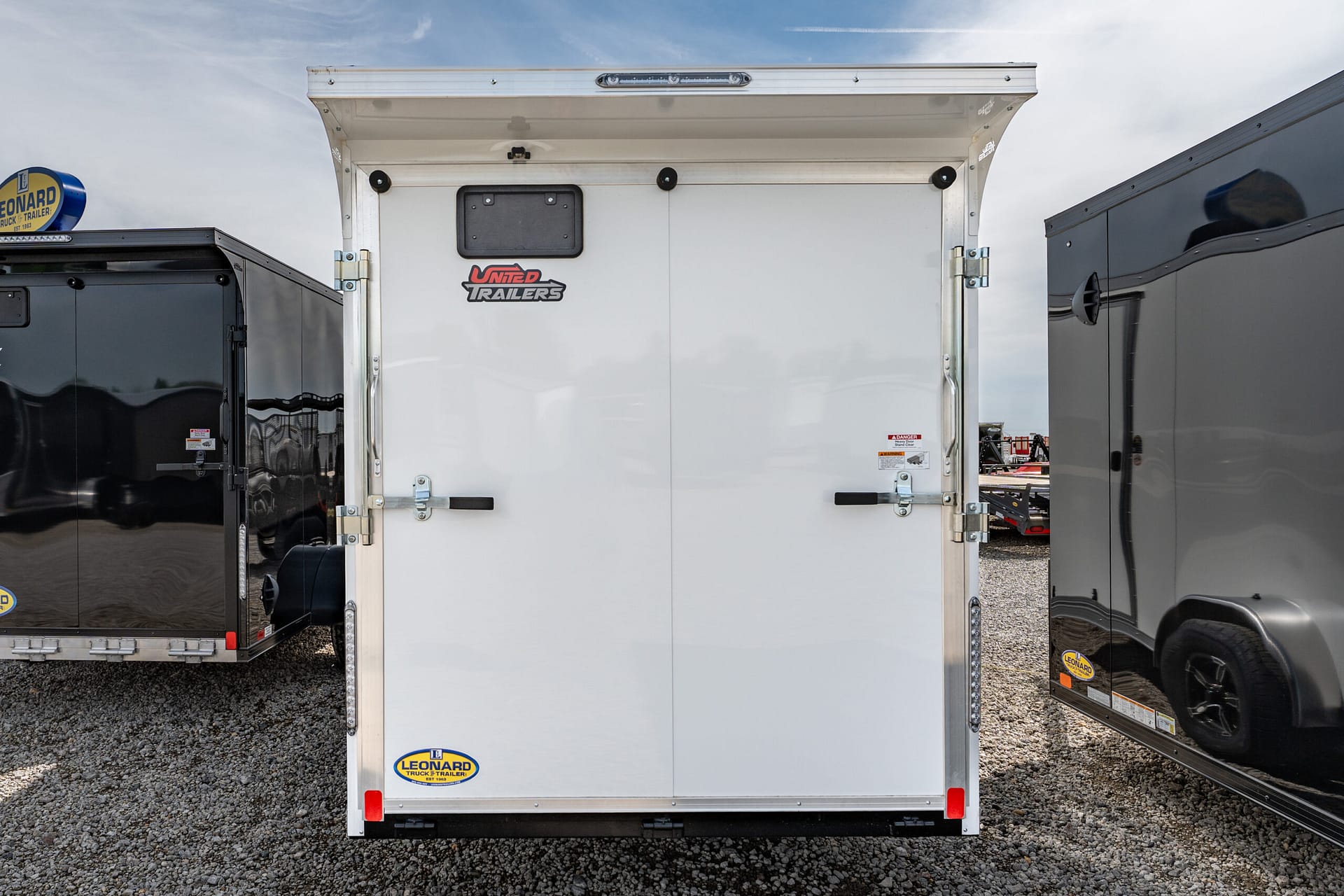 Back of a white trailer with two doors, featuring a United Trailers logo and Leonard sticker at the bottom.