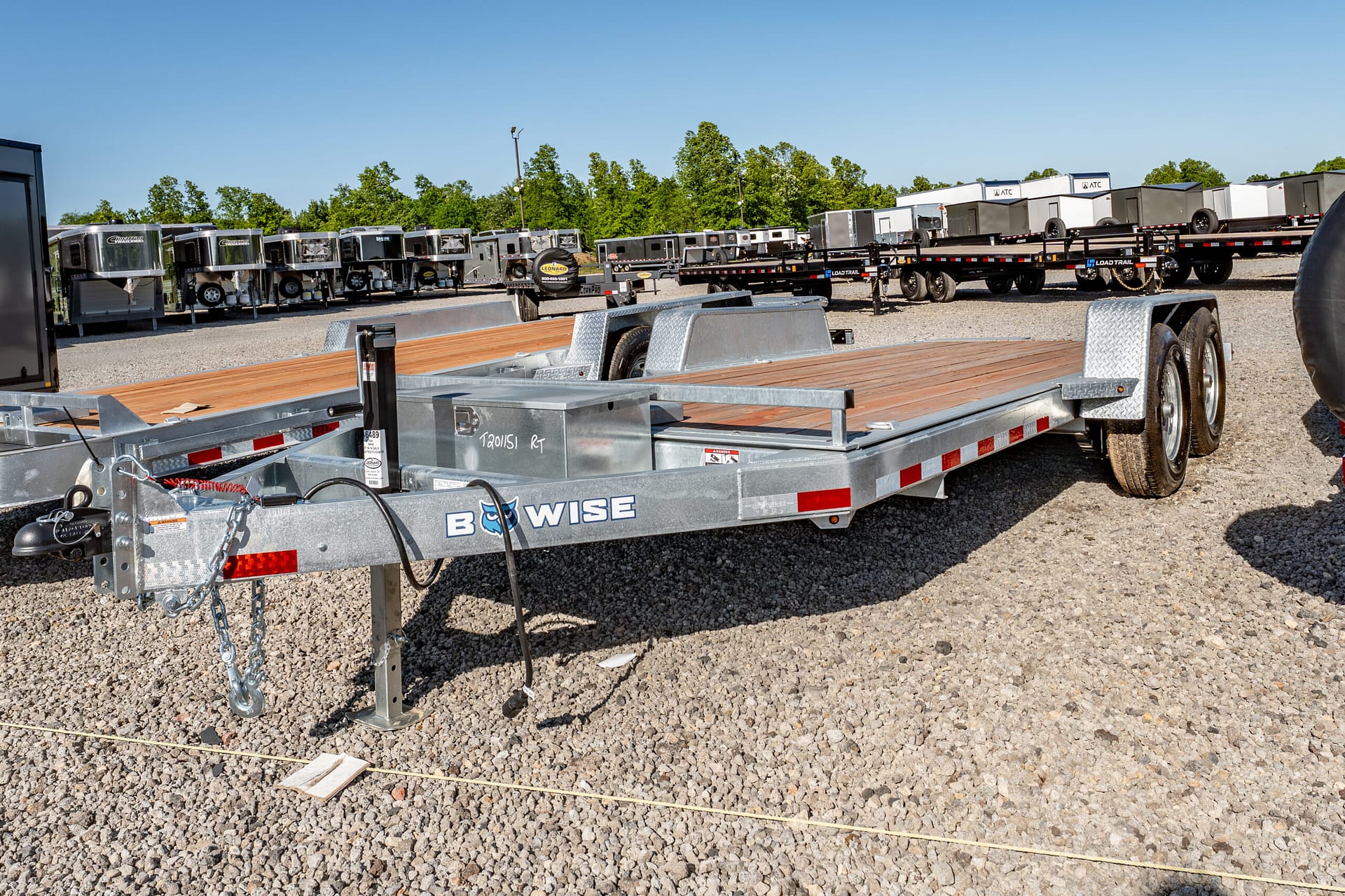 Row of silver trailers and flatbeds in a gravel lot under a clear blue sky at a trailer yard.