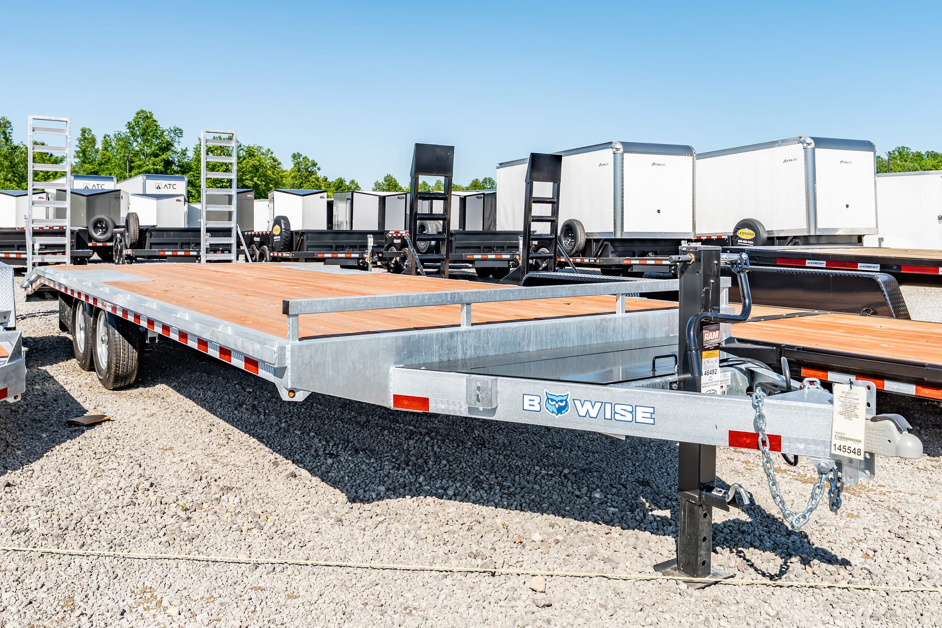 Row of flatbed trailers with wooden decks in a gravel lot under a clear blue sky.