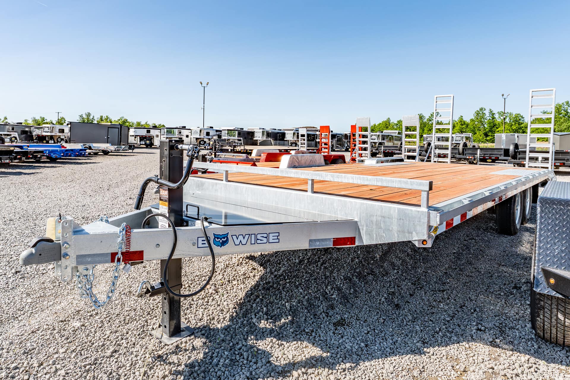 Row of flatbed trailers and equipment parked in a gravel lot under a clear blue sky at a trailer yard