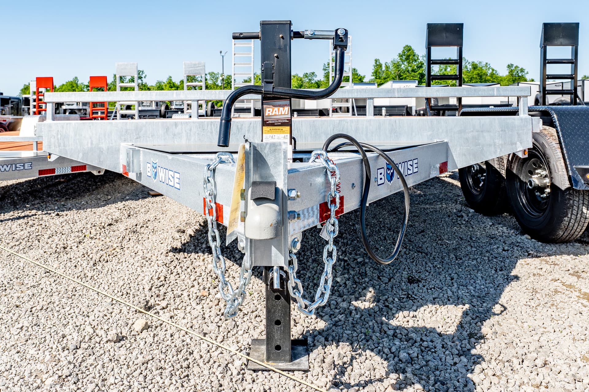 Close-up of a trailer hitch and safety chains on a metal flatbed trailer, with ladders visible in the background.