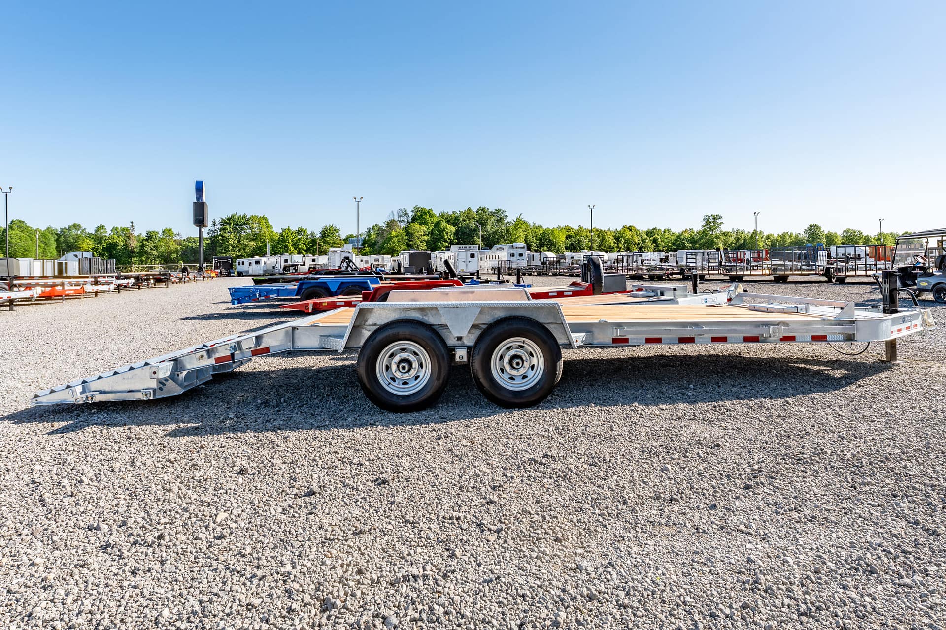 Industrial trailer yard with stacked flatbed trailers on gravel under a clear blue sky.