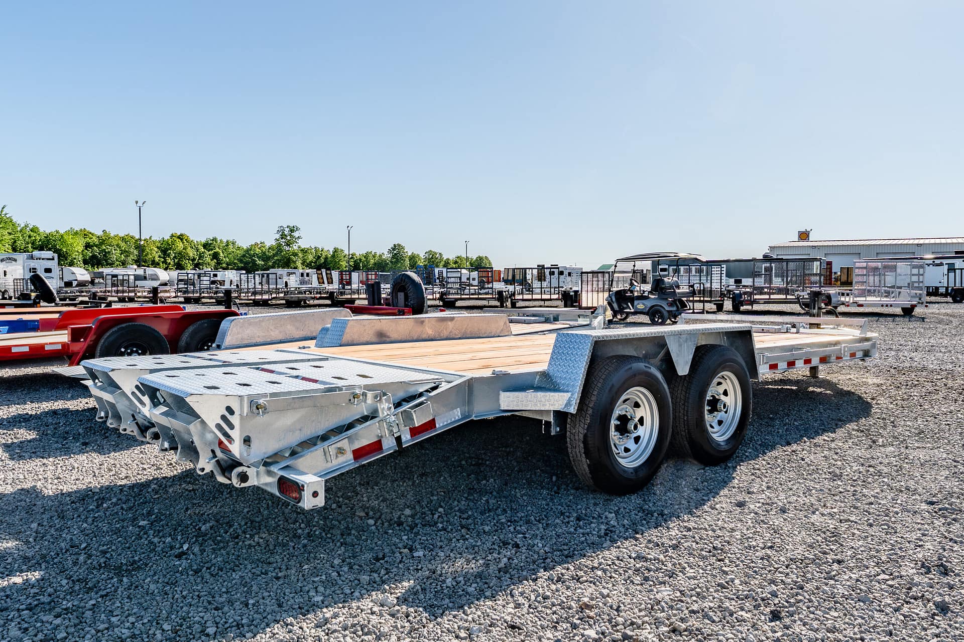 Row of flatbed trailers and other equipment parked in a gravel lot under a clear blue sky
