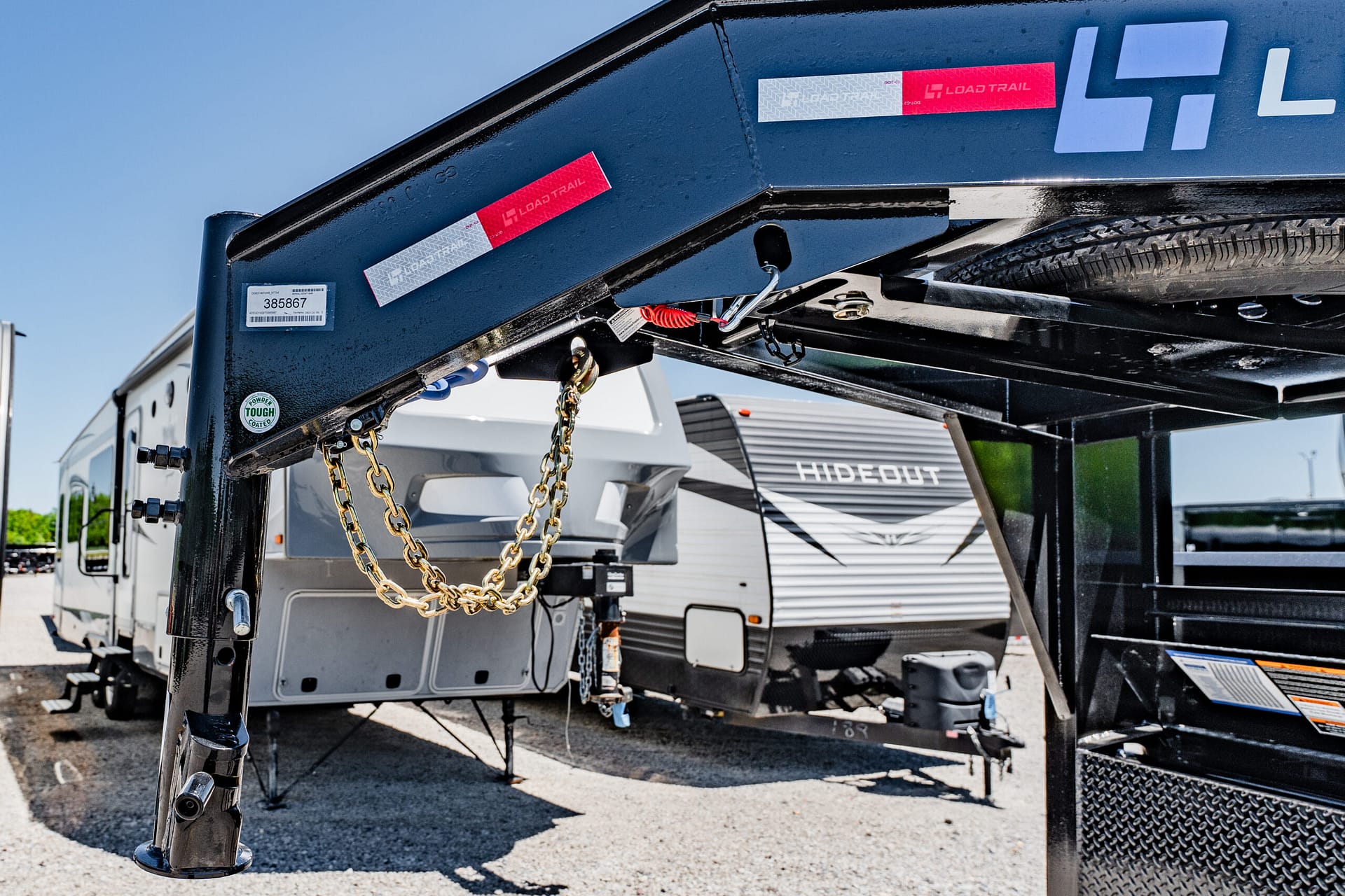 Close-up of a black trailer hitch frame with gold chains hanging, tire to the right, and red Load Trail decals visible on the side edge.