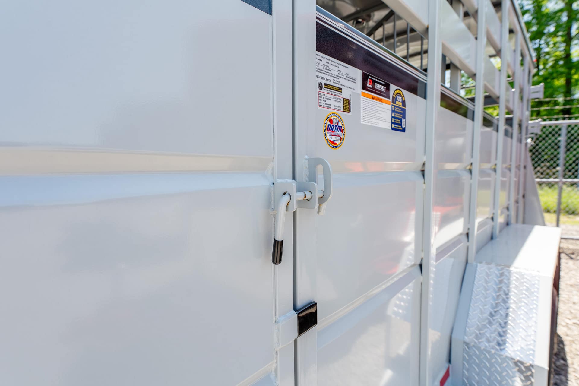 Close-up of a white utility trailer door with warning stickers and a black grab handle