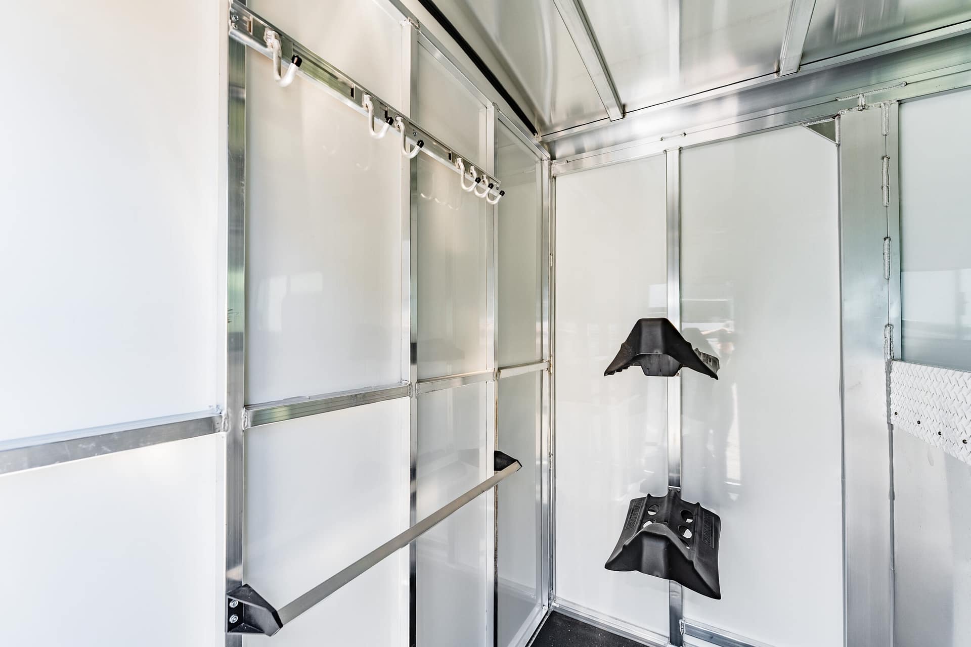 Interior of a stainless steel walk-in cooler with a row of white hooks along a ceiling rail, empty shelves nearby.