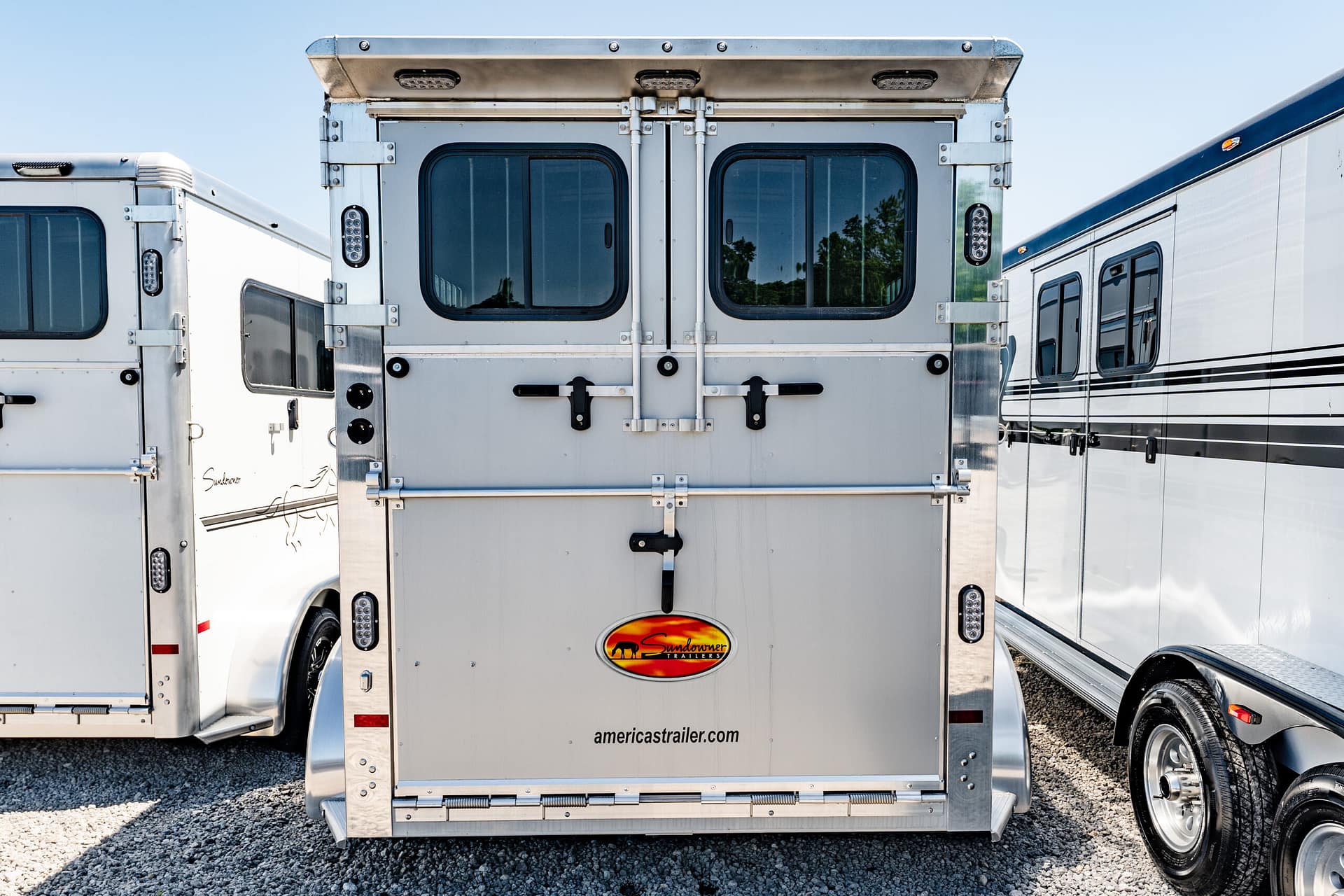 Rear view of a tall silver aluminum trailer with double back doors, latches, and a Sundowner Trailers logo on the lower tail area.