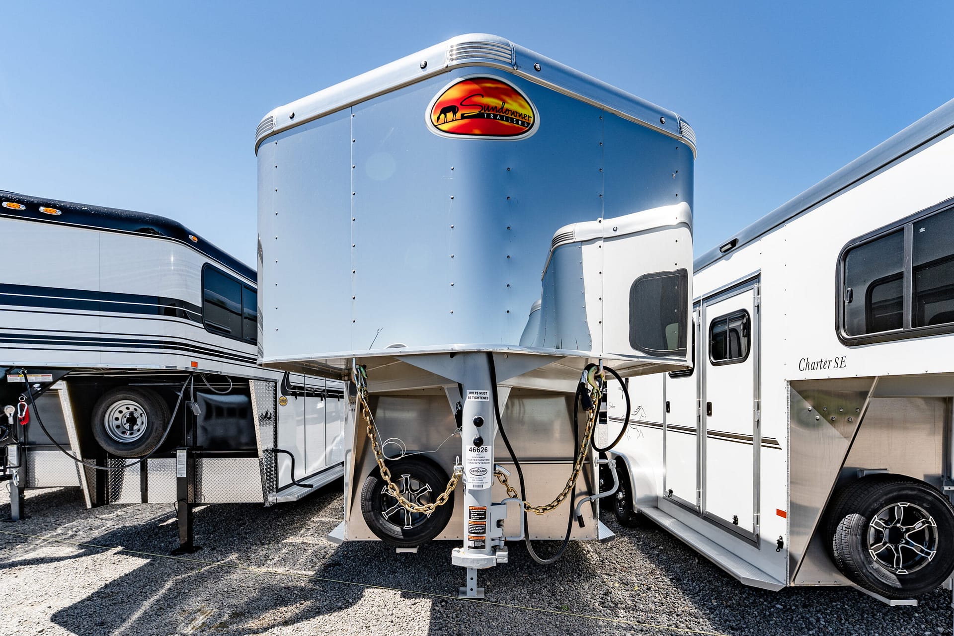 Silver aluminum trailer with Sundowner logo, parked between other trailers under a clear blue sky.