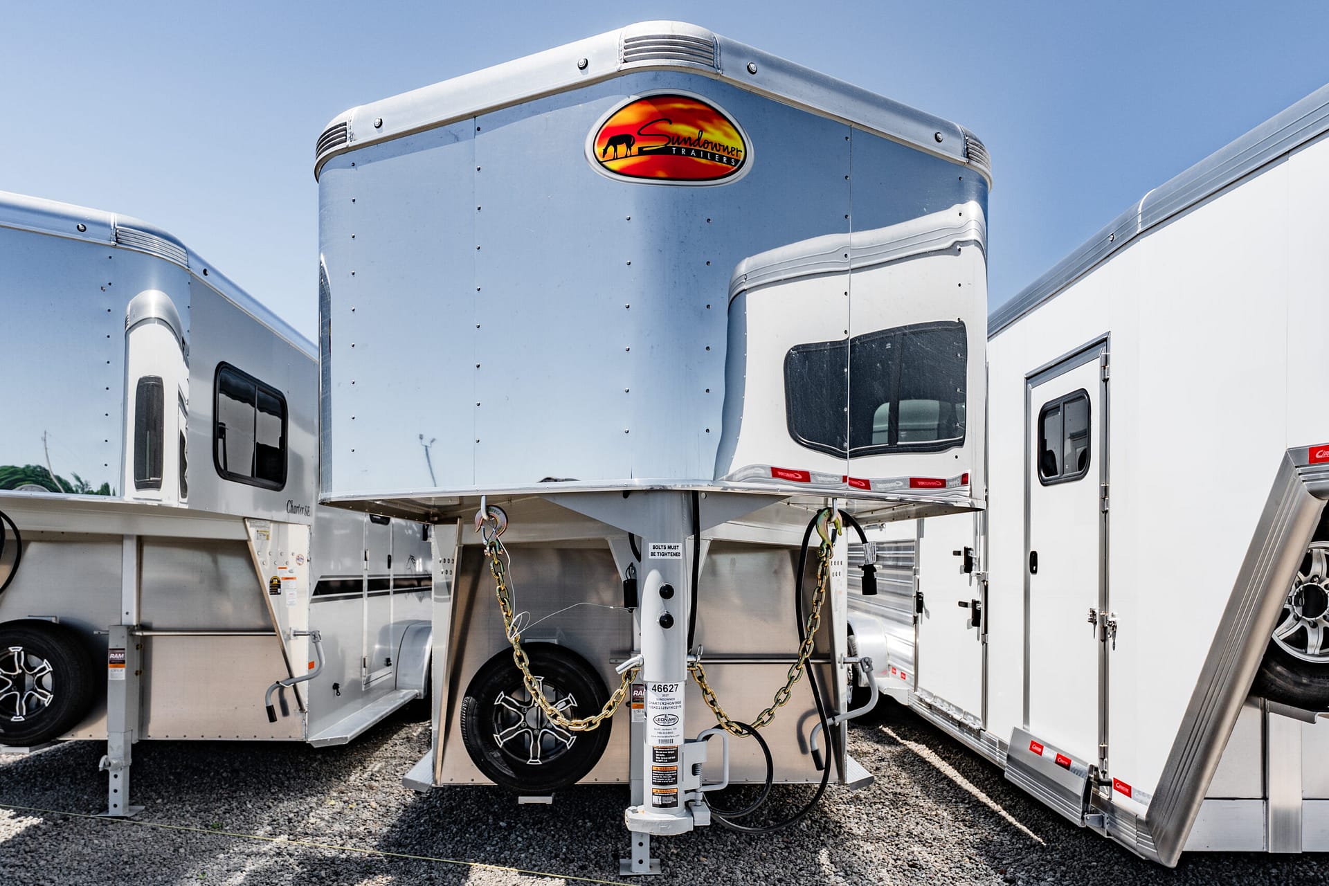 Shiny aluminum trailer front with a red-orange Sundowner Trailers logo and blue sky above