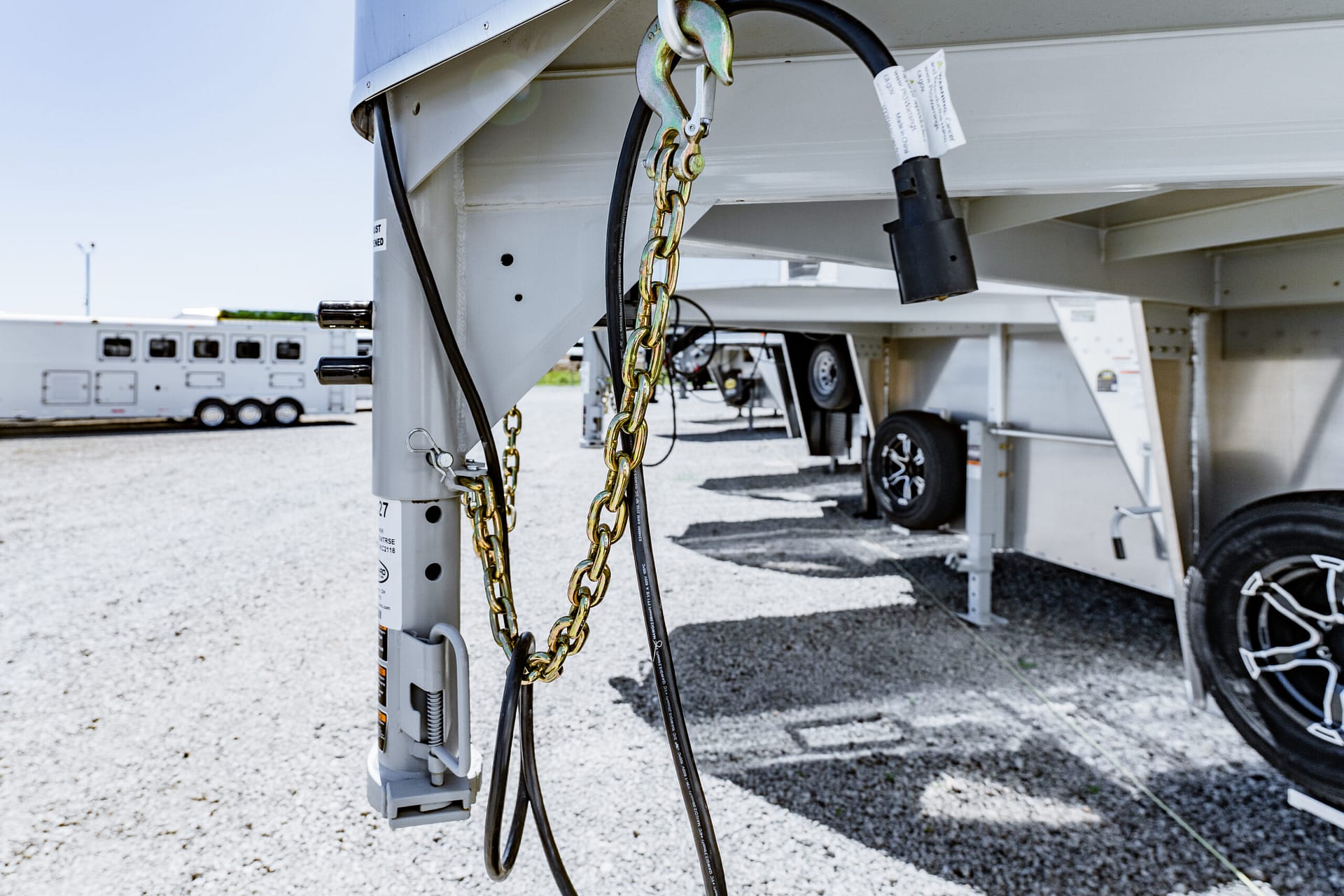 Chains, cables, and hitch components securing a trailer undercarriage in a gravel lot.