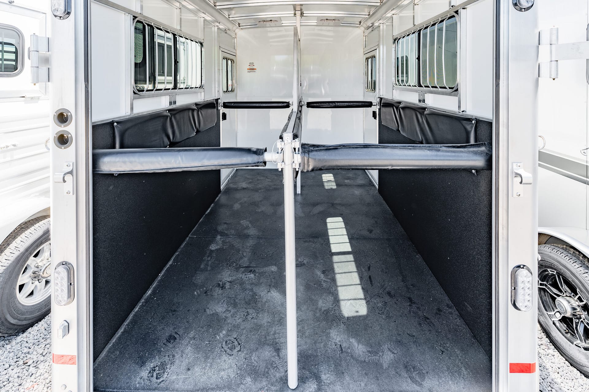 Interior of a white horse trailer showing two empty stalls with black padded walls and metal dividers.