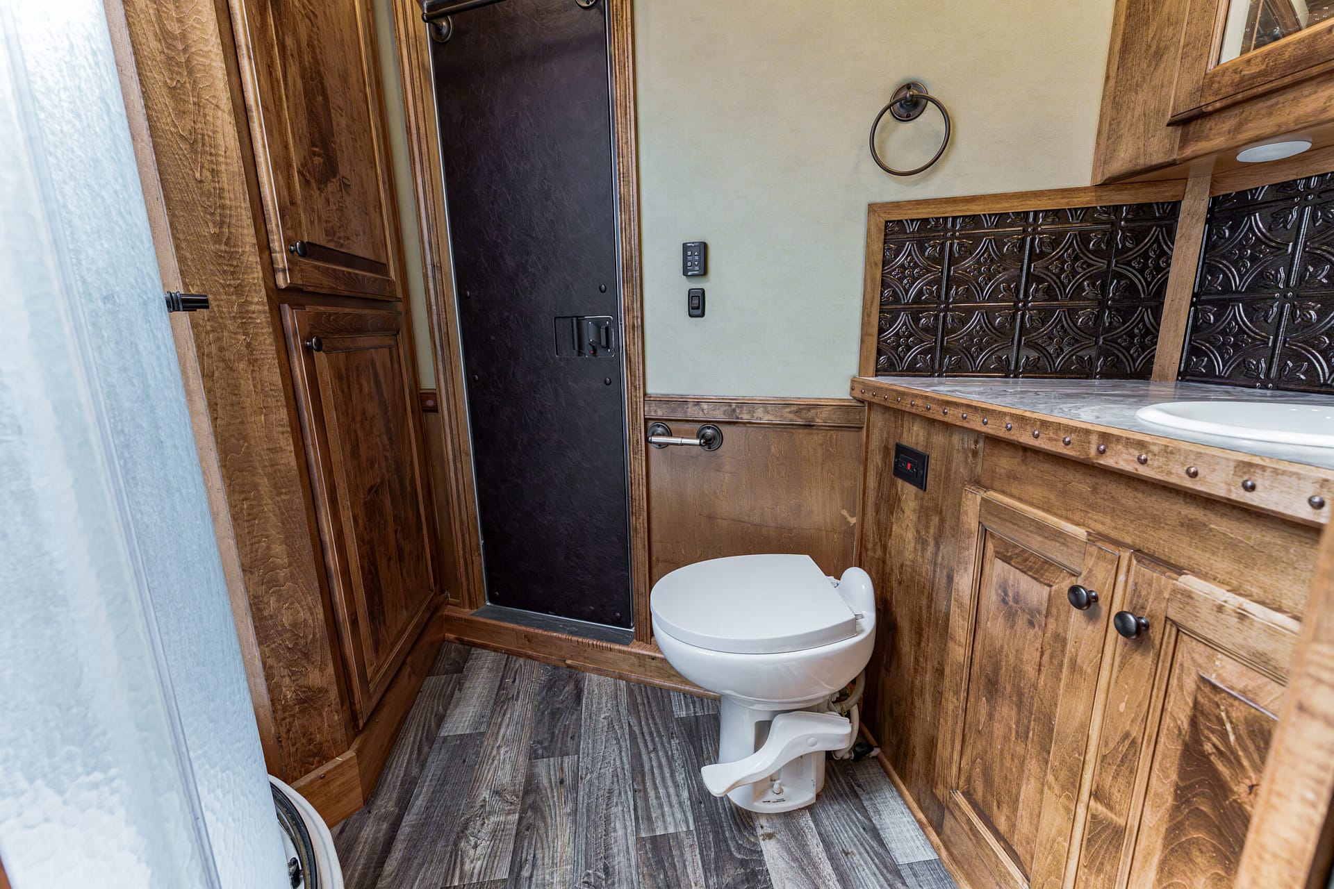 RV bathroom with wood cabinets, beige walls, and a white toilet beside a marble-topped counter; circular towel ring on the wall.