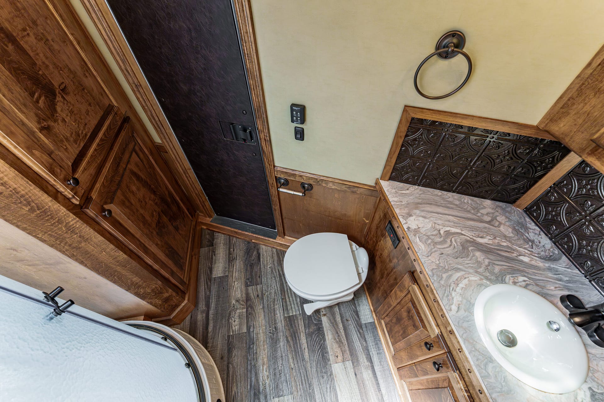 Compact bathroom in a rustic wooden RV: toilet, sink, and dark wood cabinets with a beige wall and circular towel ring above the counter.