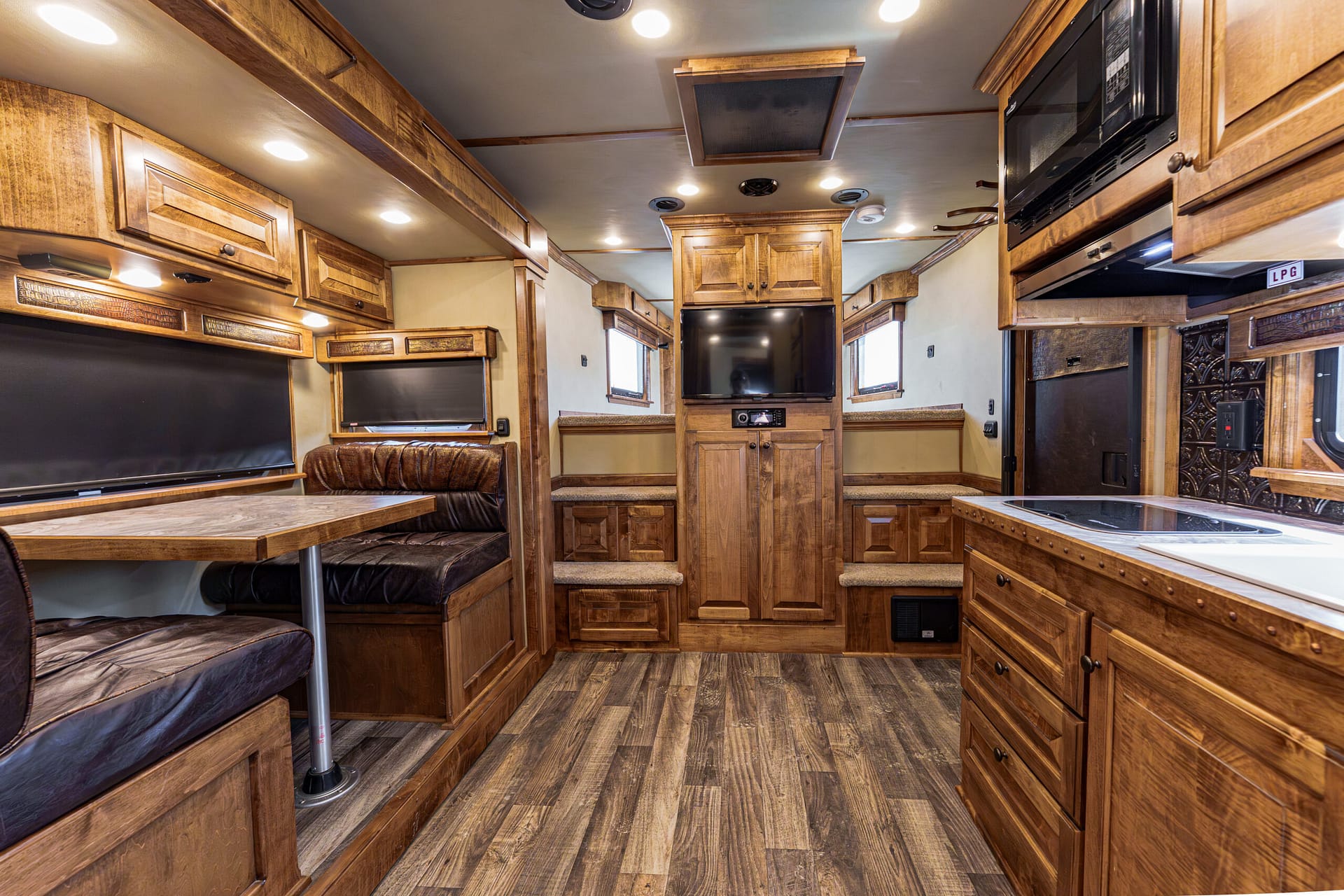 Wood-paneled RV interior with a dinette, cushioned seating, and upper cabinets surrounding a central TV. The space feels cozy and well-lit.
