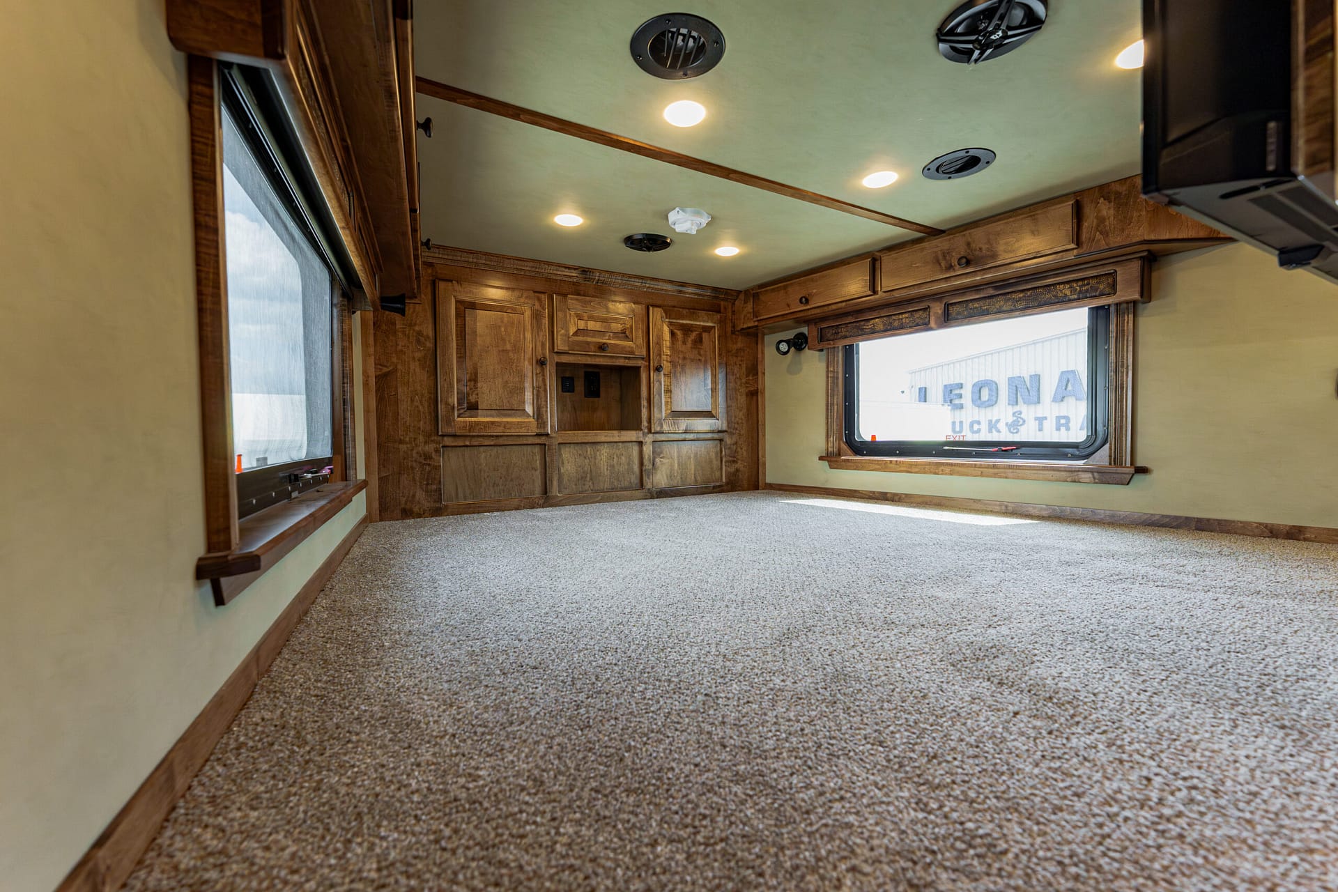 Interior of an RV living area with wooden cabinets, a window, and ceiling lights; carpeted floor shows through.