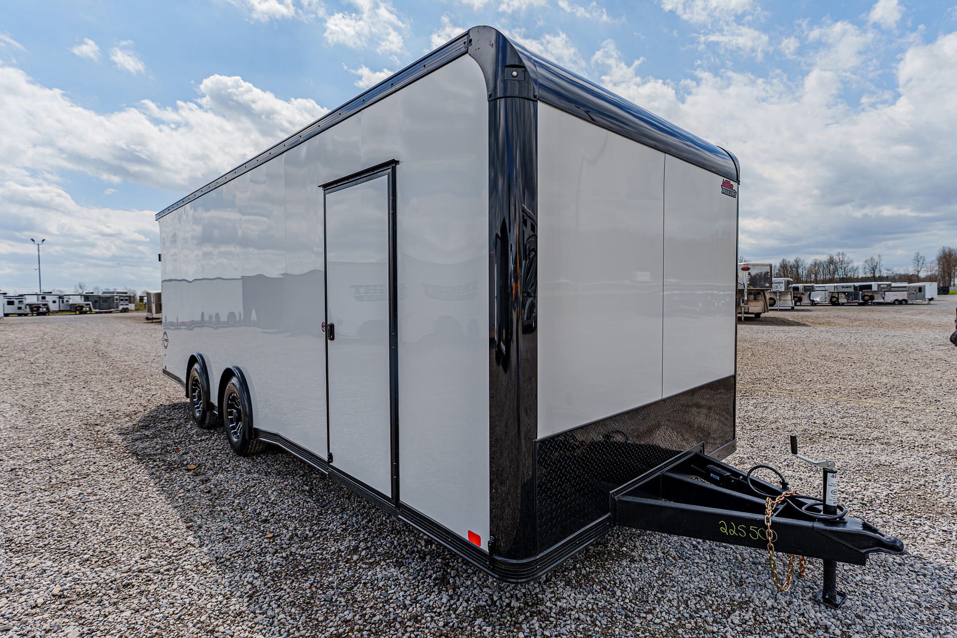 Large white enclosed trailer with a black front corner, parked on a gravel lot under a cloudy sky.