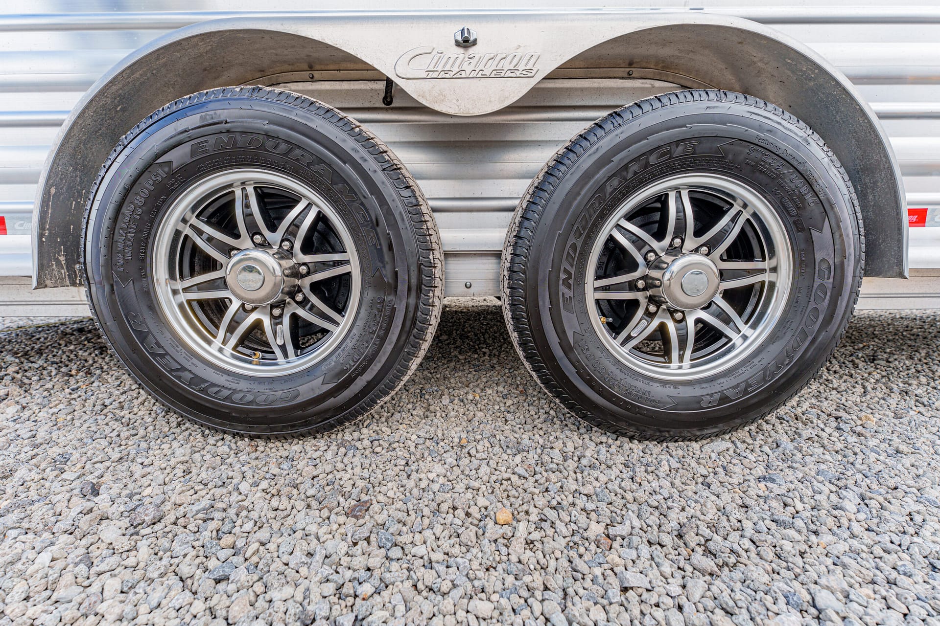 Two trailer wheels with chrome rims and Goodyear Endurance tires, set on a gravel surface under a metal trailer fender.