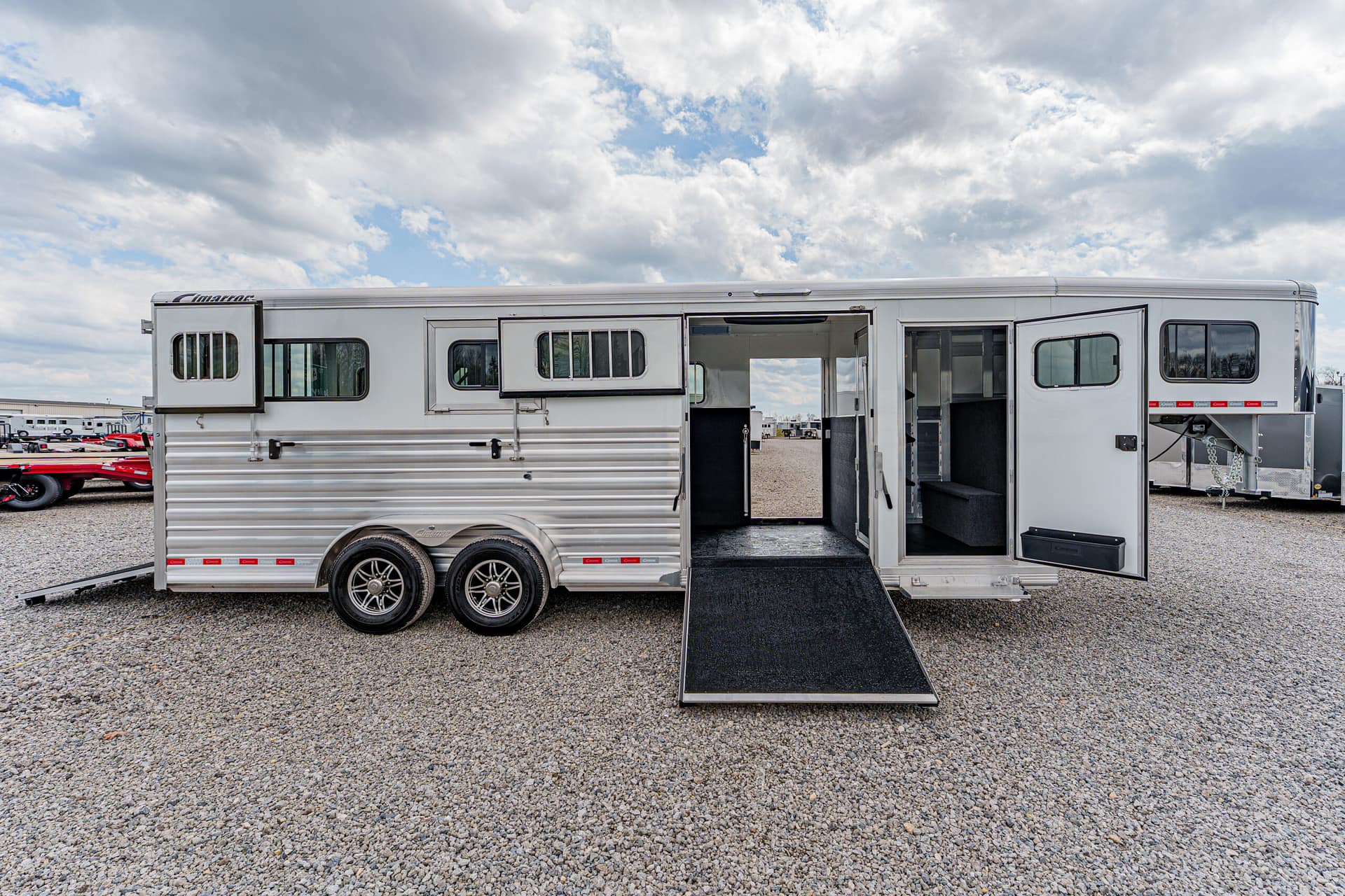 Two‑axle aluminum horse trailer with ramp down on a gravel lot