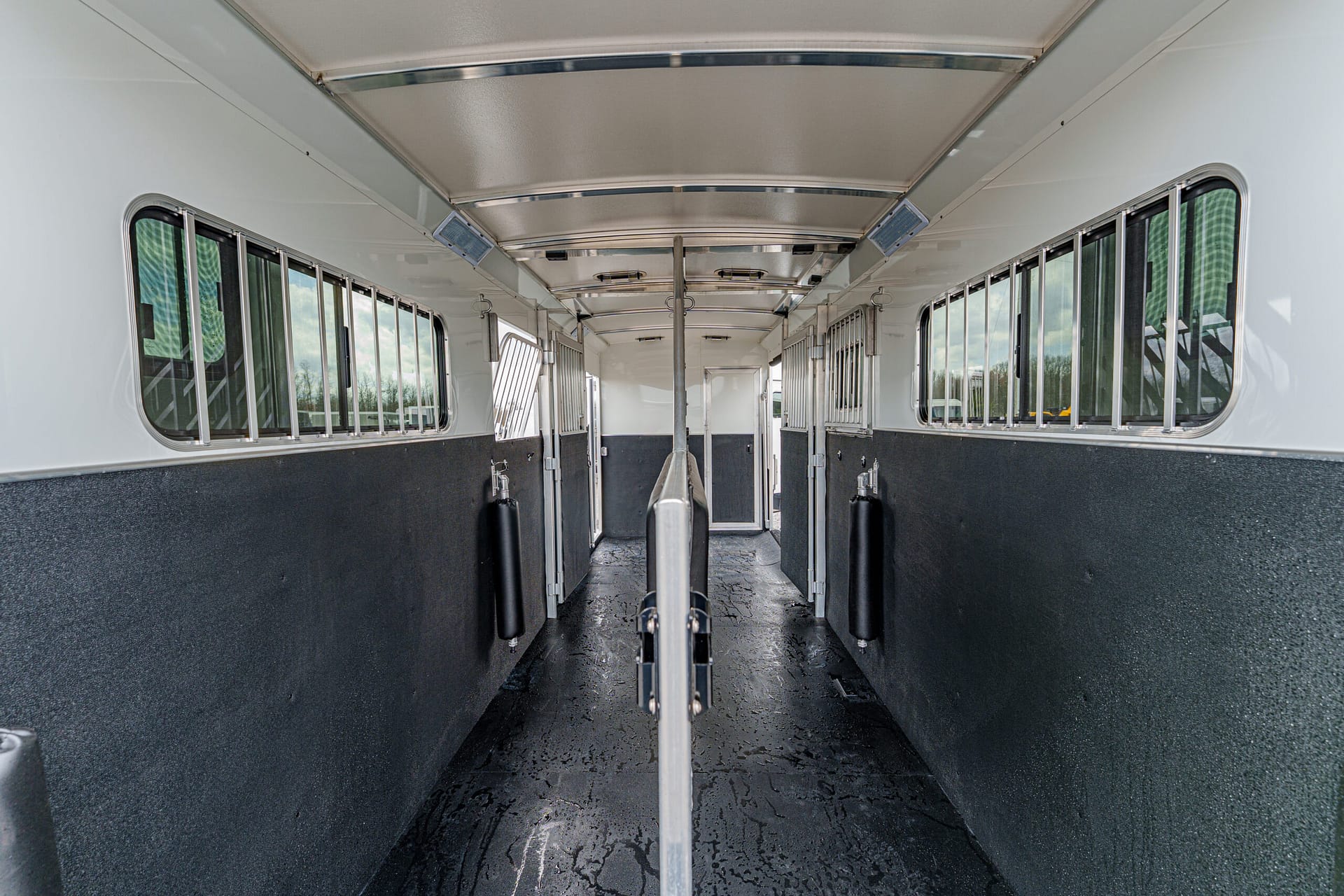 Interior of a horse trailer with a central divider, white upper walls, dark lower panels, and windows with bars along both sides