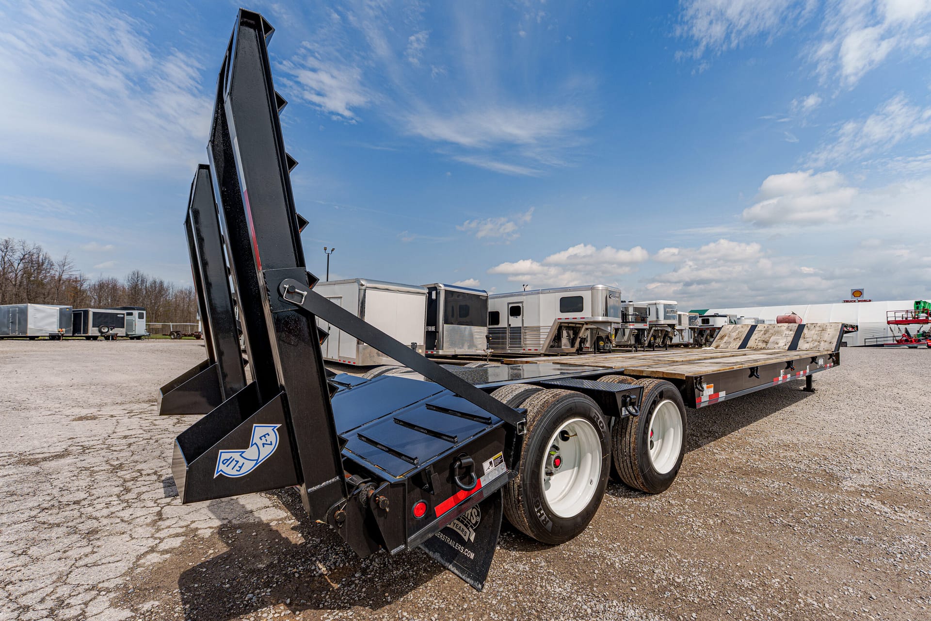 Flatbed trailer with raised loading ramps in a truck yard, blue sky and other trailers in the background