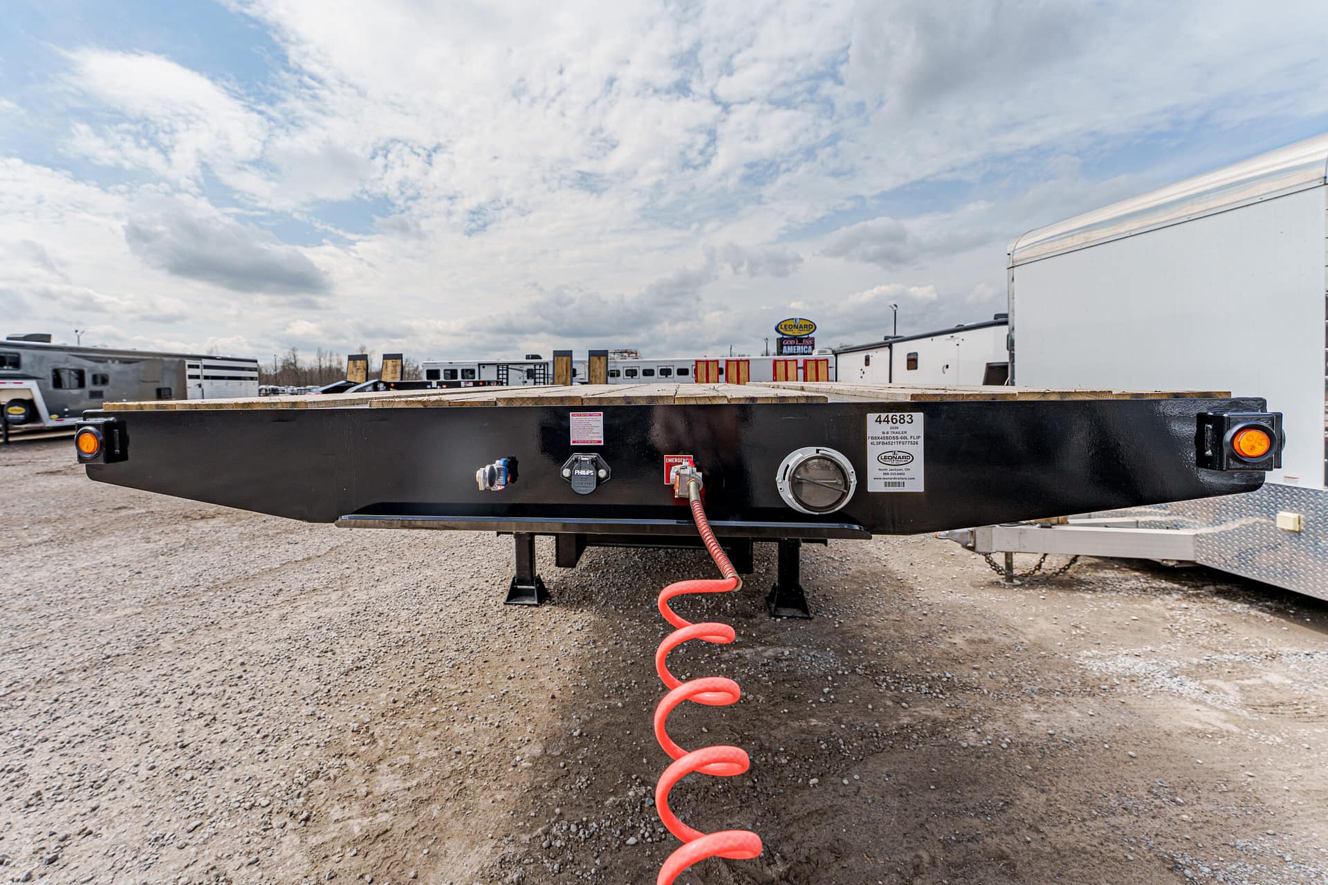 Black flatbed trailer with a red coiled air hose connected to a valve, in a trailer yard with other rigs nearby