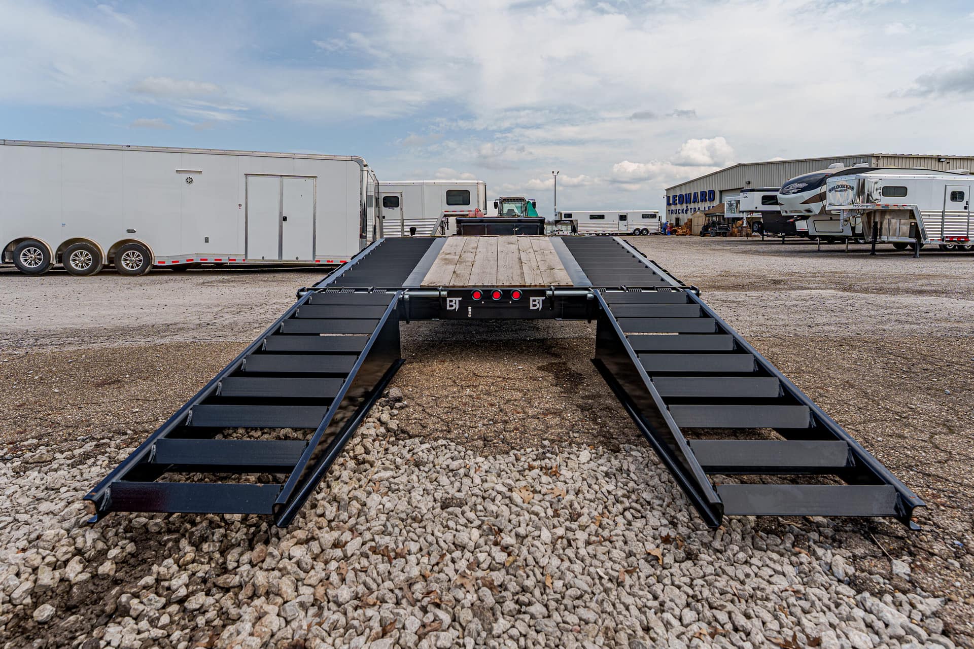Wide shot of a heavy-duty trailer with two side ramps extending from a central platform in a truck yard.