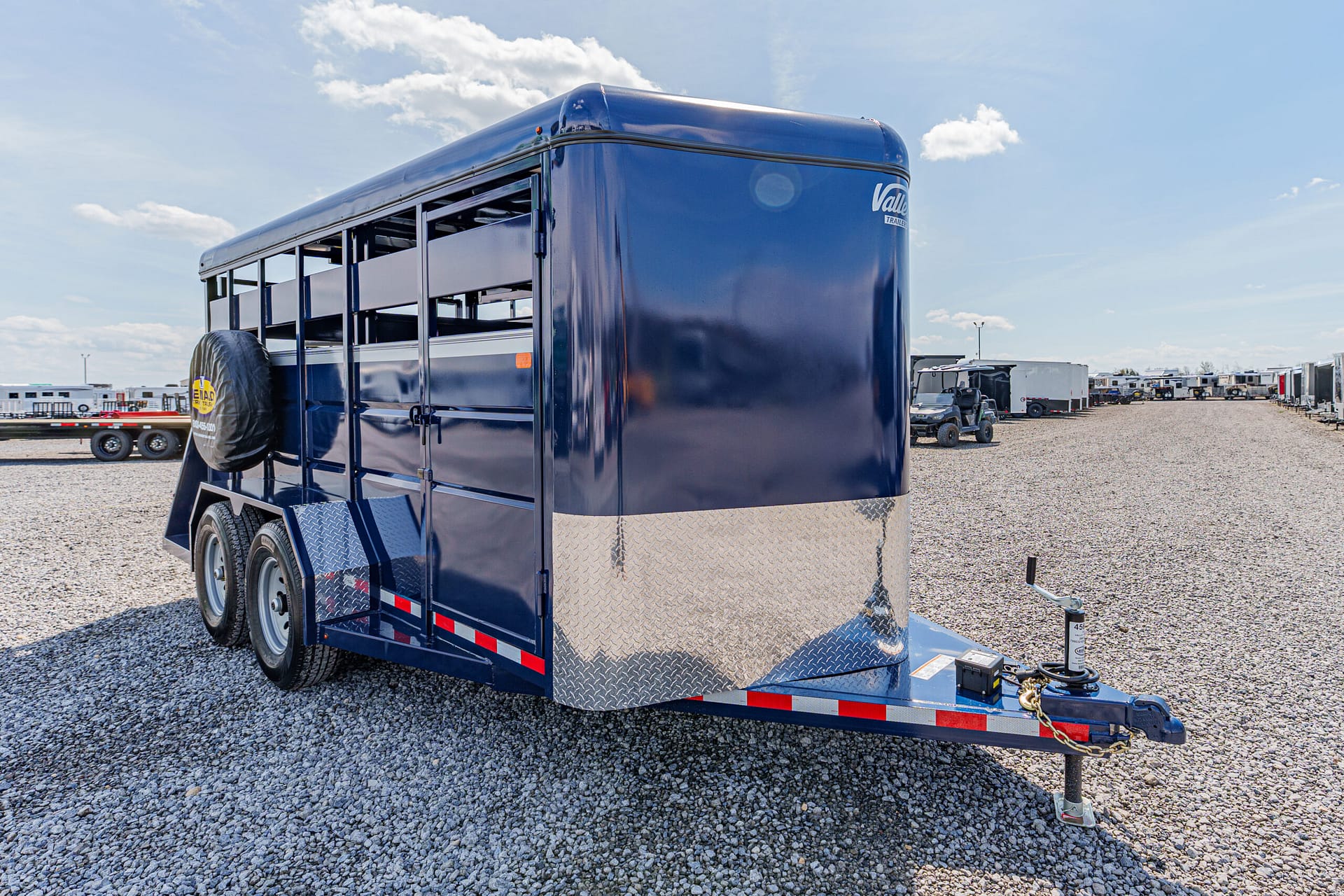 Blue livestock trailer on a gravel lot, with a spare tire mounted on the side and diamond-plate front.