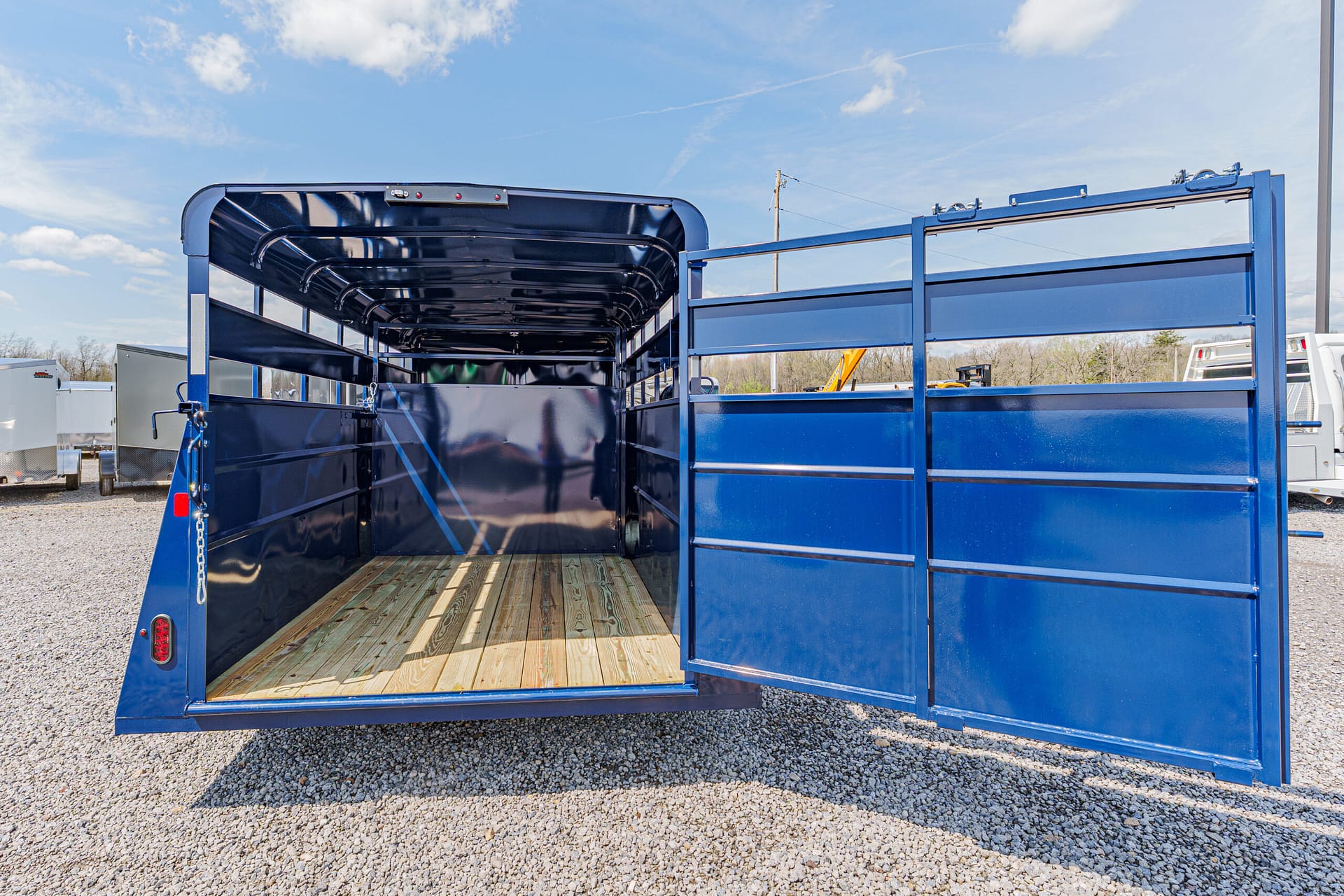 Blue livestock trailer with open rear ramp, empty interior and wood plank floor on a gravel lot