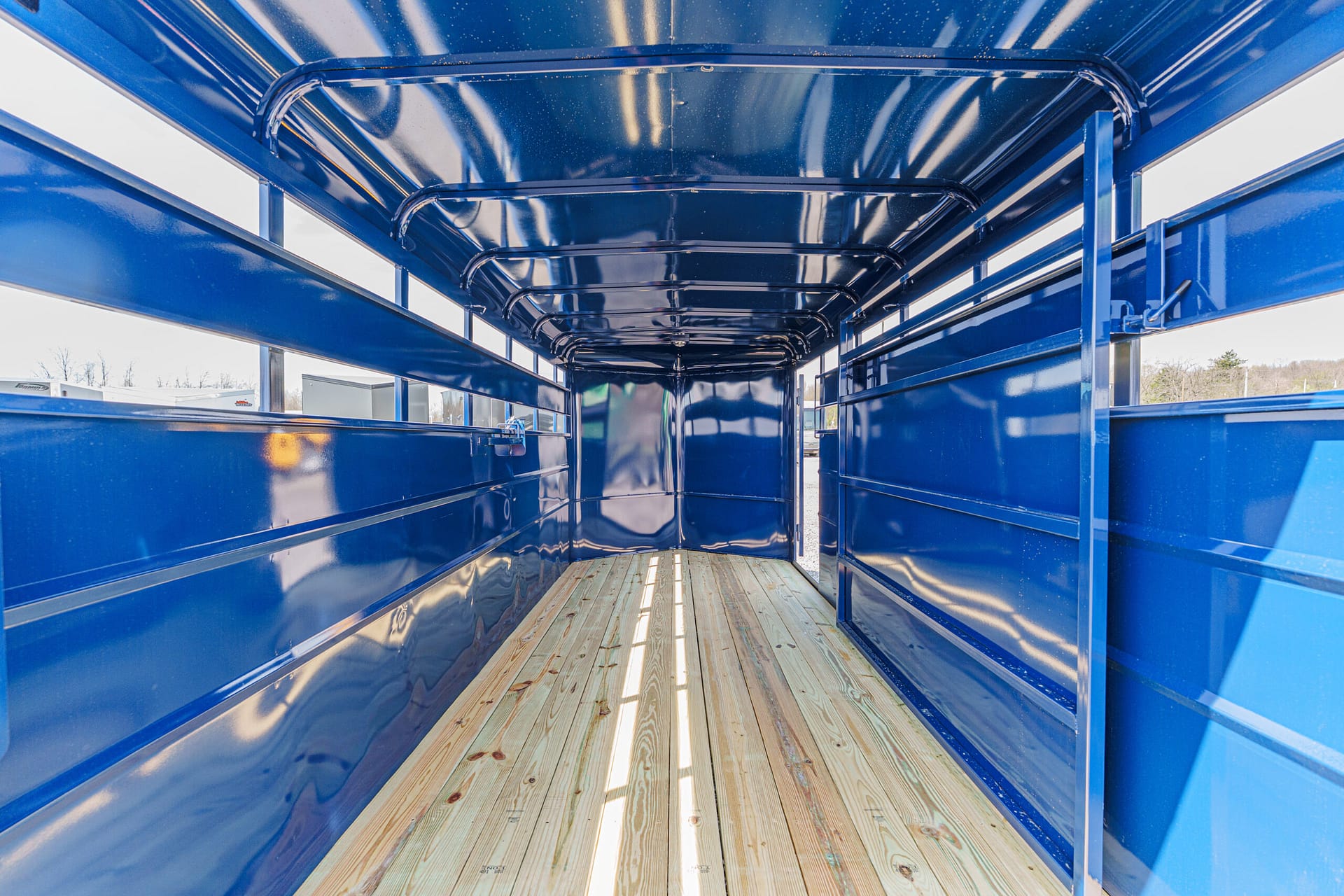 Interior of a blue metal trailer with a wooden floor, viewed toward the rear opening