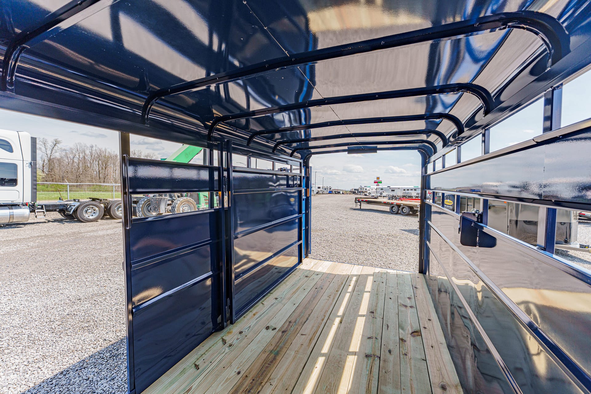 Interior of an empty blue trailer with a wooden floor, viewed from the back toward a truck yard and other trailers.
