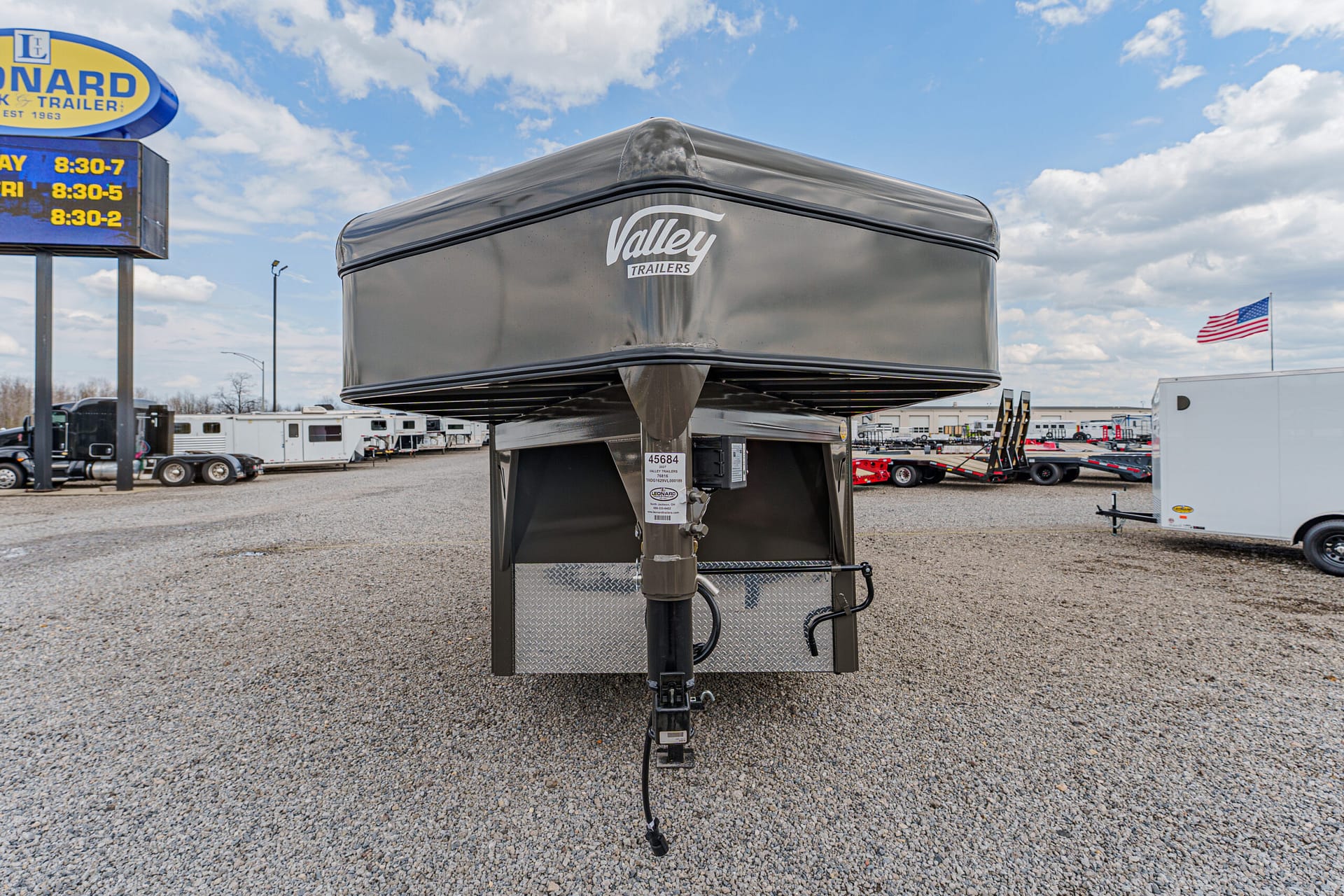 Front view of a gray Valley Trailers gooseneck trailer with hitch, parked on a gravel lot at a trailer dealership.