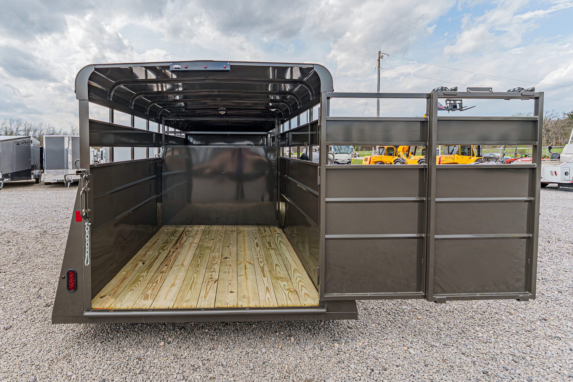 Open horse trailer interior with wooden floor and black metal walls, parked on a gravel lot