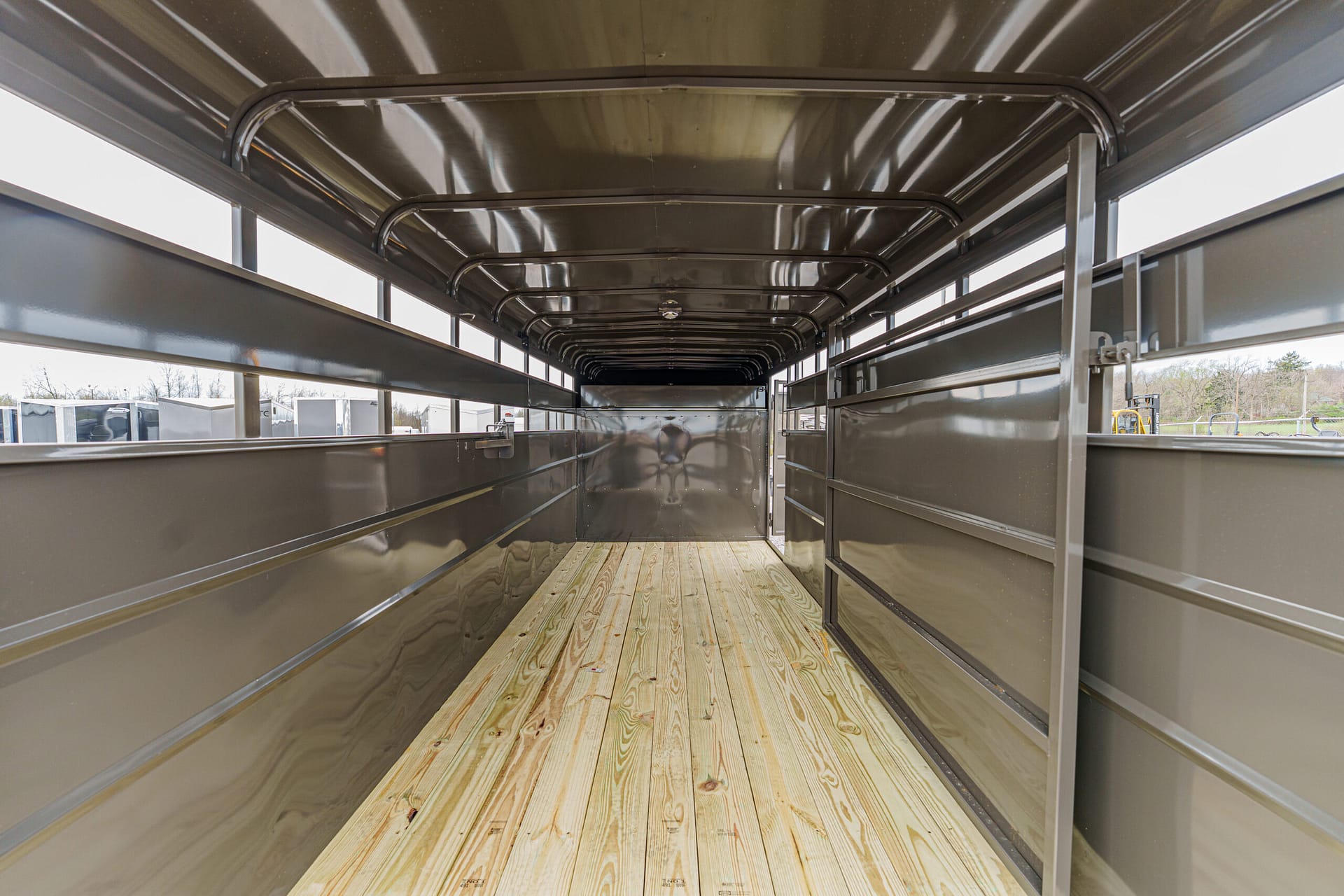 Interior of an empty gray metal trailer with a wooden plank floor, viewed from inside toward the rear.