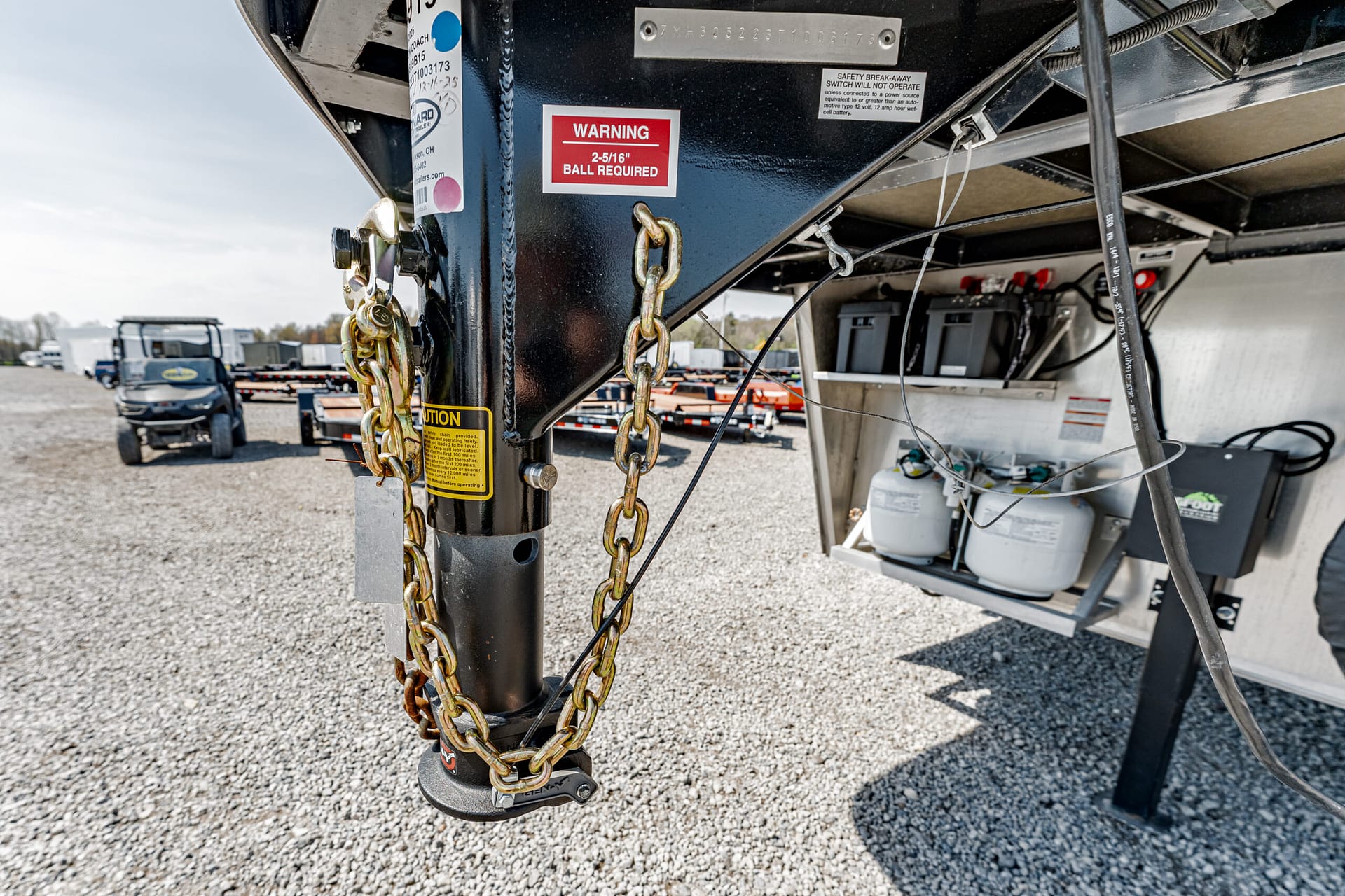Close-up of a trailer hitch with heavy chains and wiring, black metal frame, warning sticker visible on the front.
