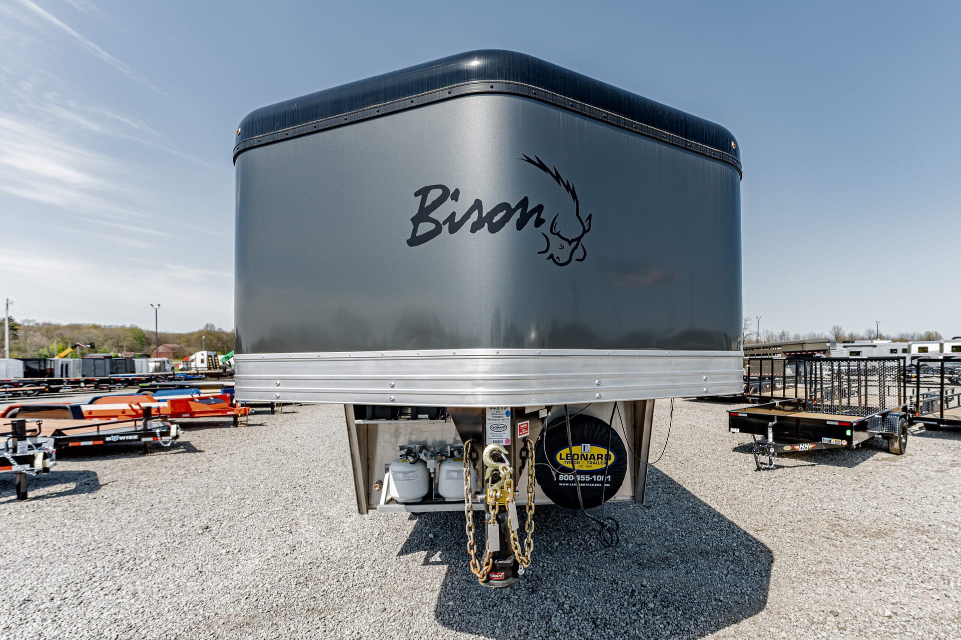 Gray Bison-brand trailer with logo, parked in a gravel lot among other trailers (front/hitch area visible).