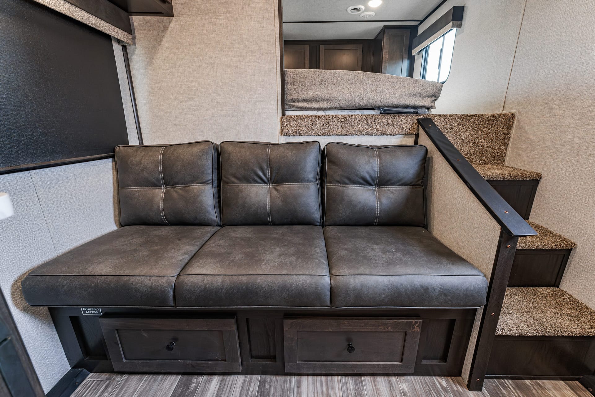 Dark gray leather sofa in a compact RV living area with a staircase to a loft bunk ahead.
