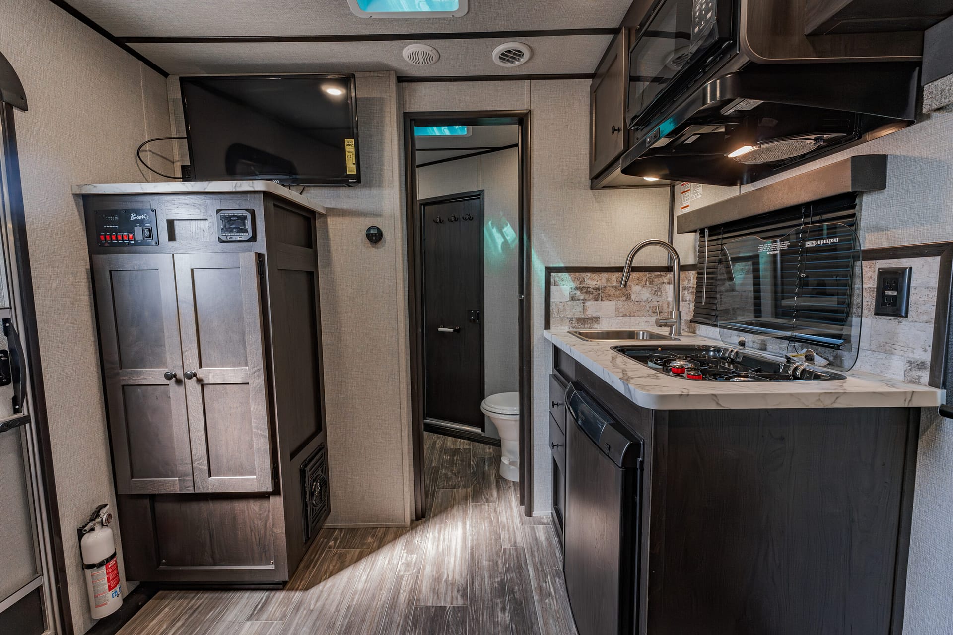 Interior of an RV kitchen with dark cabinets, countertop, sink, stove, and microwave along a U-shaped view.