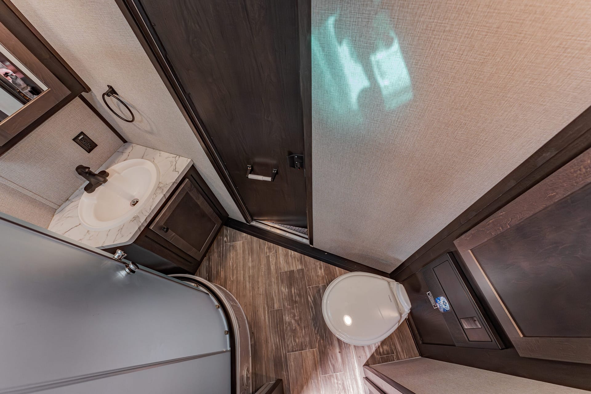 Compact RV bathroom: sink with marble countertop, dark wood vanity, and toilet next to a curved shower enclosure.