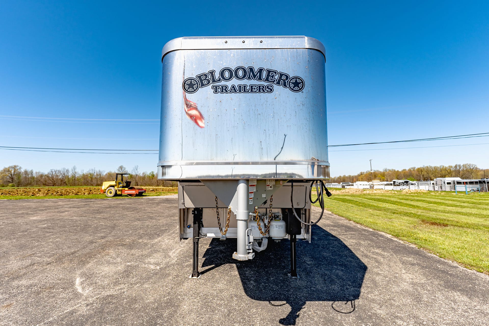 Large silver trailer with the words 'BLOOMER TRAILERS' painted on its front, parked on a paved lot under a clear blue sky.