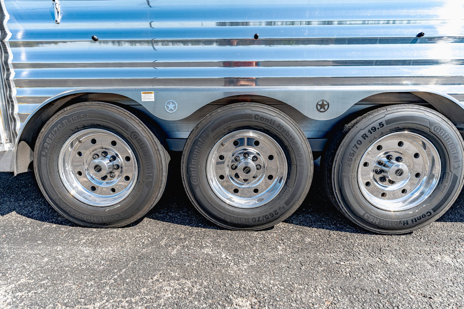 Close-up of three shiny trailer wheels on a silver corrugated trailer faceplate.