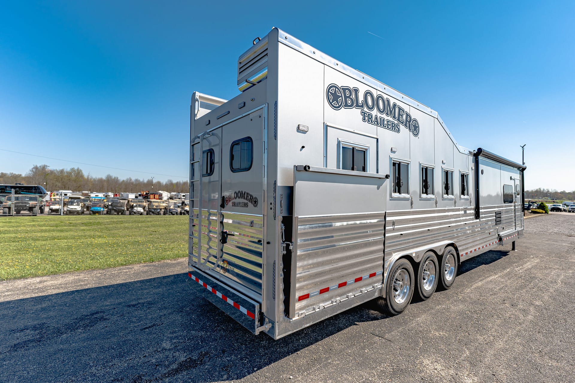Silver aluminum trailer with 'Bloomers Trailers' branding parked in a sunny lot; multiple wheels and riveted sides visible.