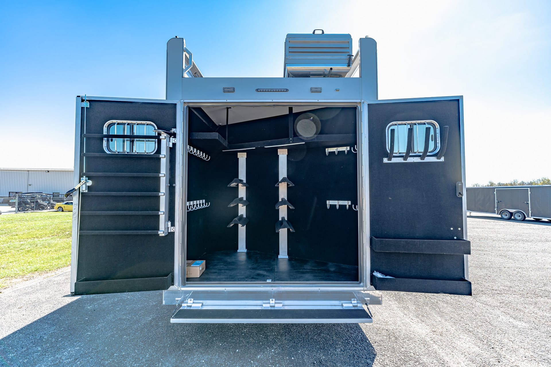 Open rear of a large black trailer with its doors wide, showing an empty dark interior with two tall vertical metal rails and blades for loading or processing equipment.