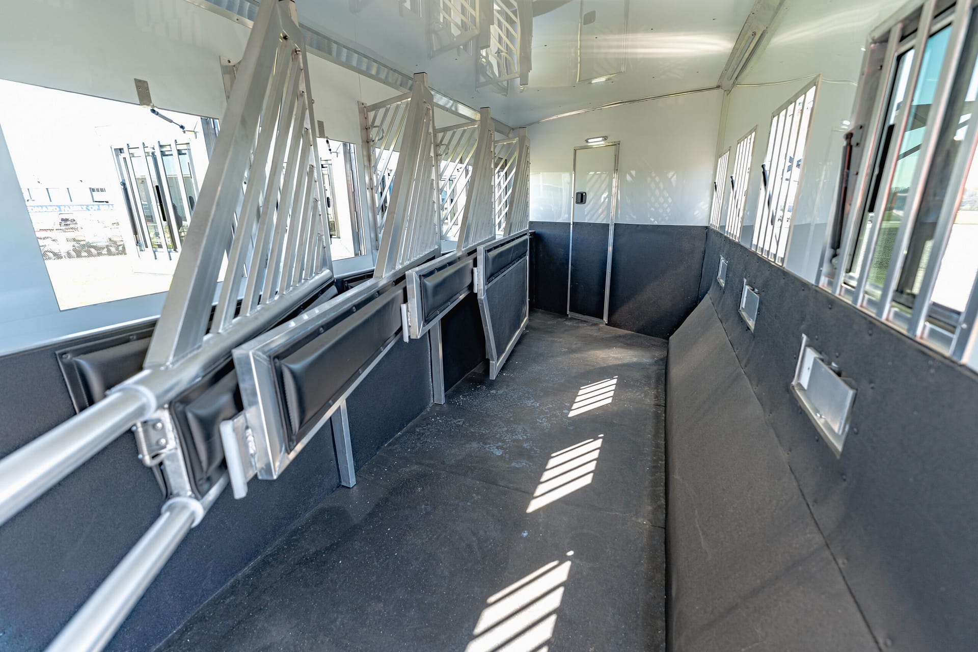 Interior of an empty transport vehicle with metal partition rails and long black benches along both walls, window light patterns on the floor