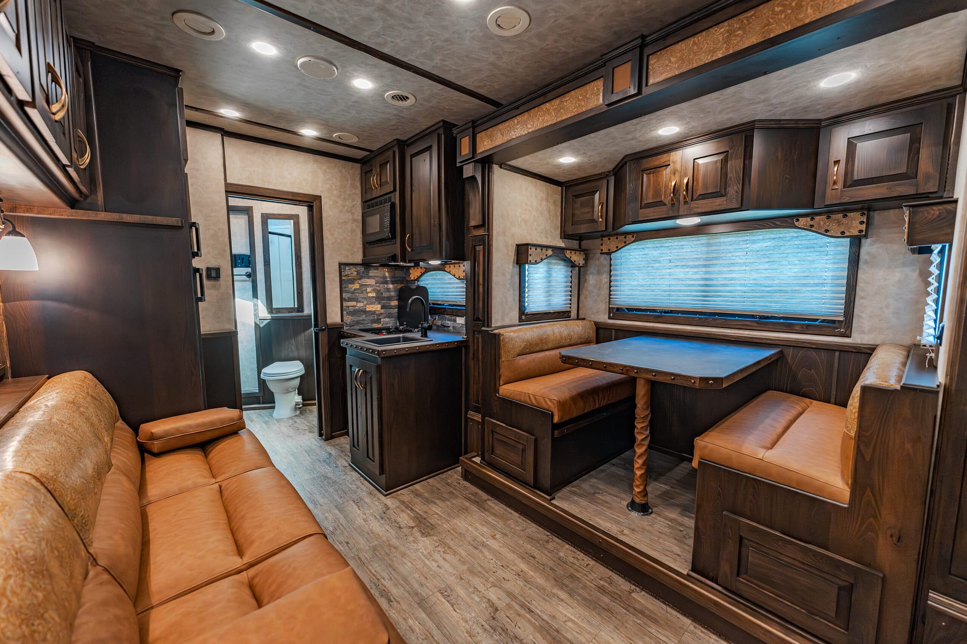 Interior of a dark-wood RV with brown leather seating, a dining table, and built-in cabinets.