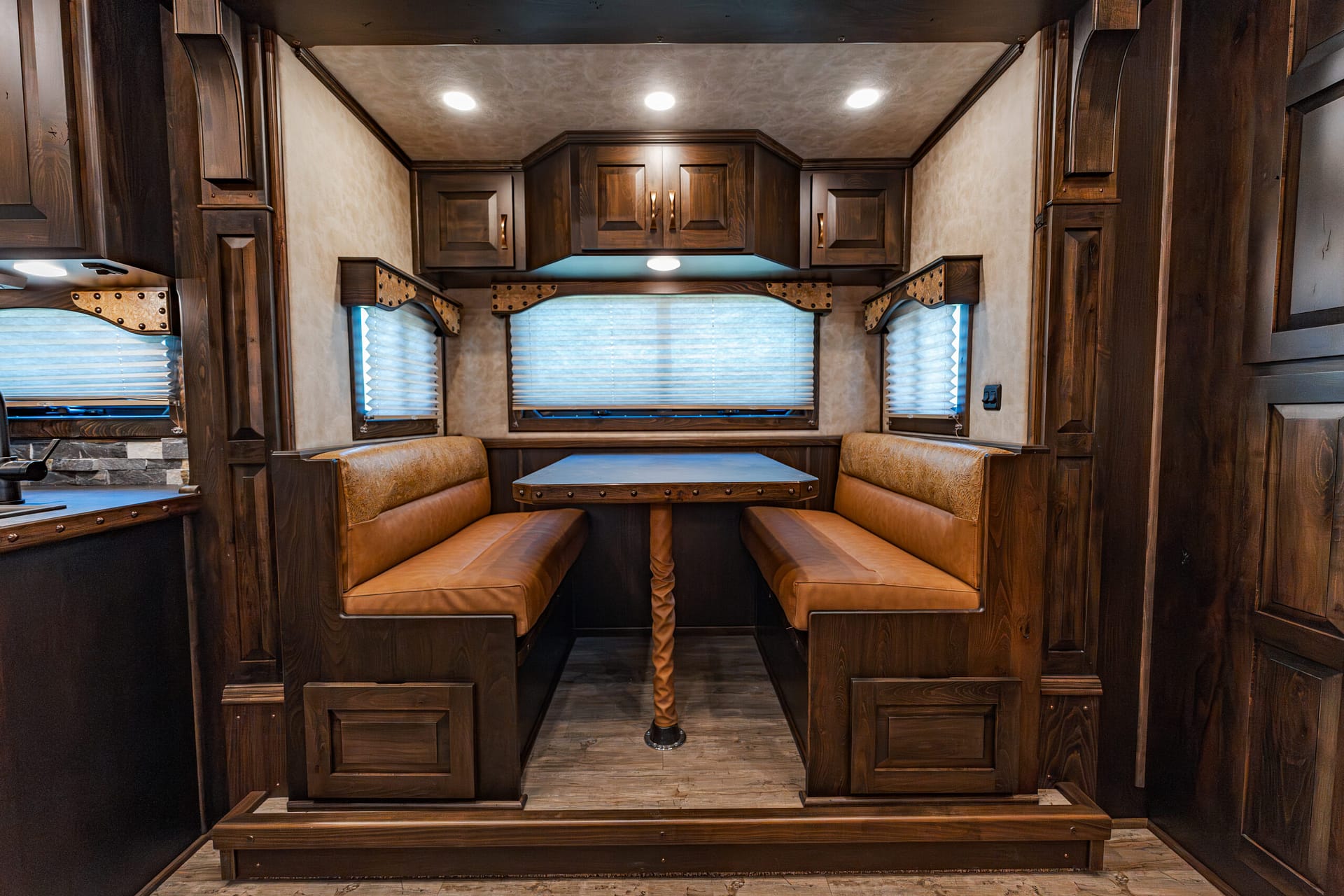 Wood-paneled RV dining nook with brown leather benches, central table, and overhead cabinets.