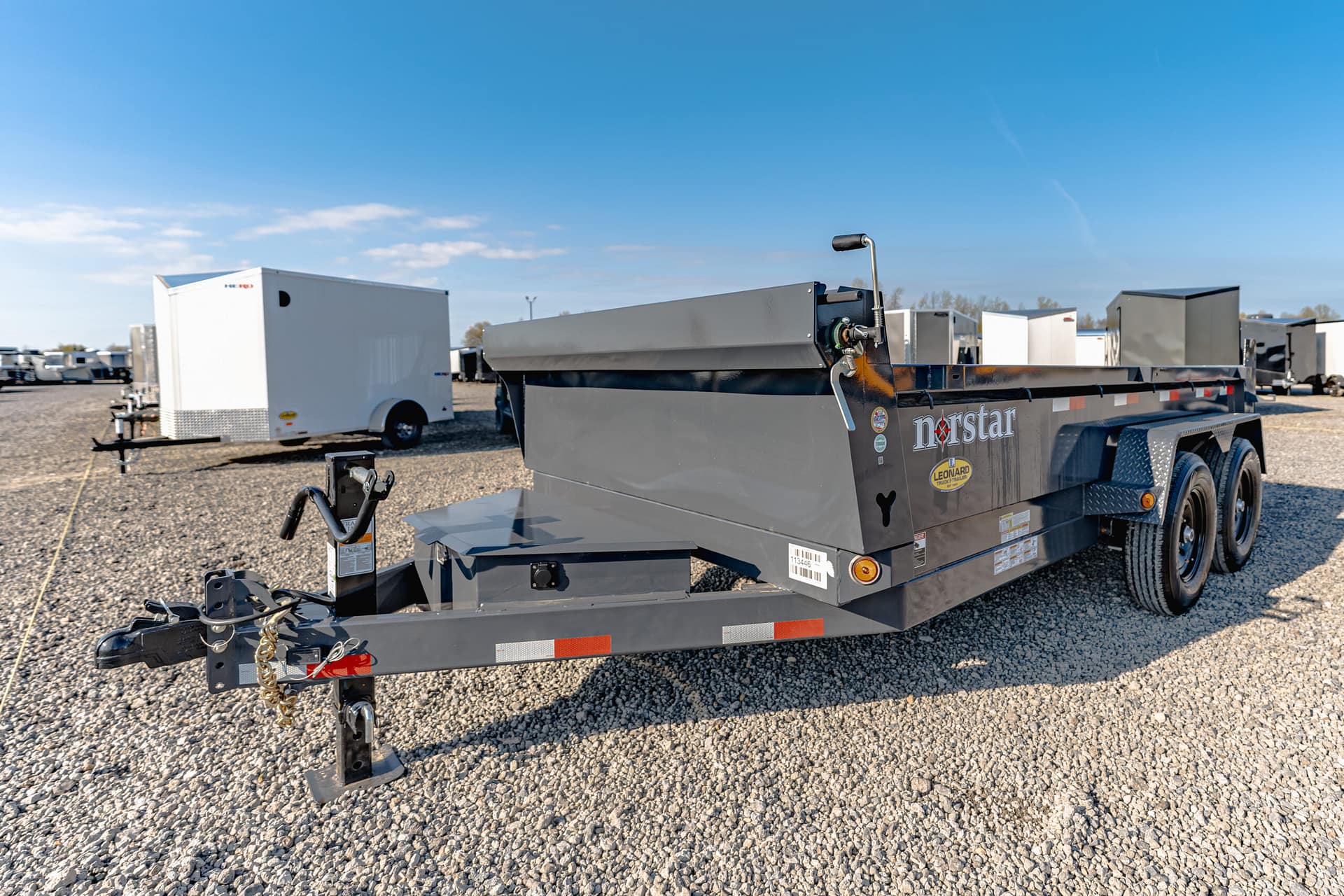 Grey flatbed trailer on a gravel lot with a blue sky and other trailers in the background, suggesting a truck yard or dealership.