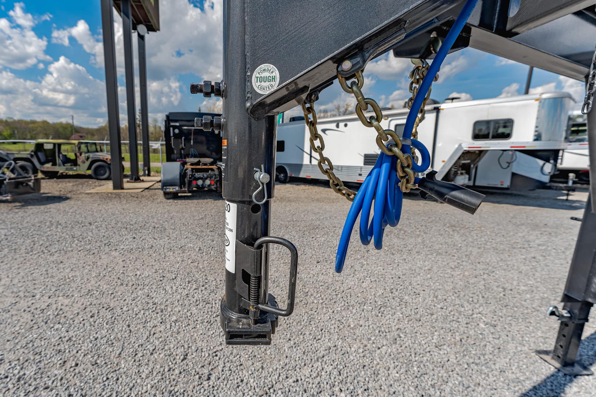 Close-up of a trailer hitch with chains and blue cables attached to a black metal frame, outdoor storage yard in the background.