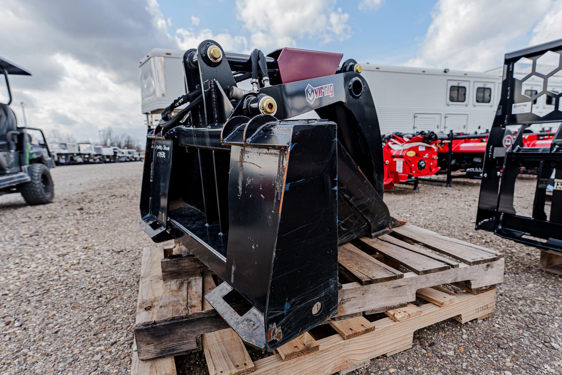 Large black hydraulic grapple attachment resting on a wooden pallet outdoors.