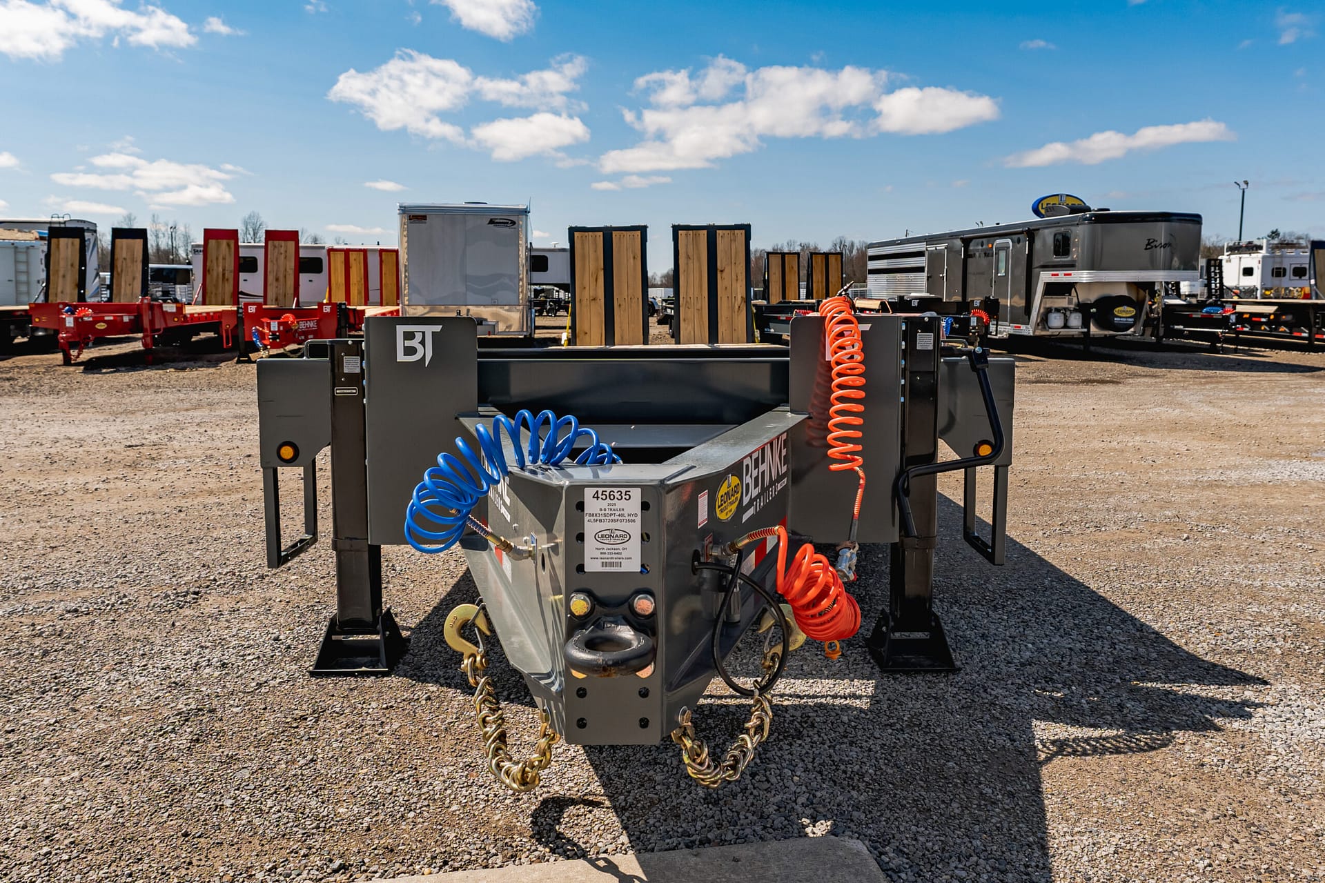 Industrial trailer with orange and blue coiled hoses in a gravel lot at a truck yard.